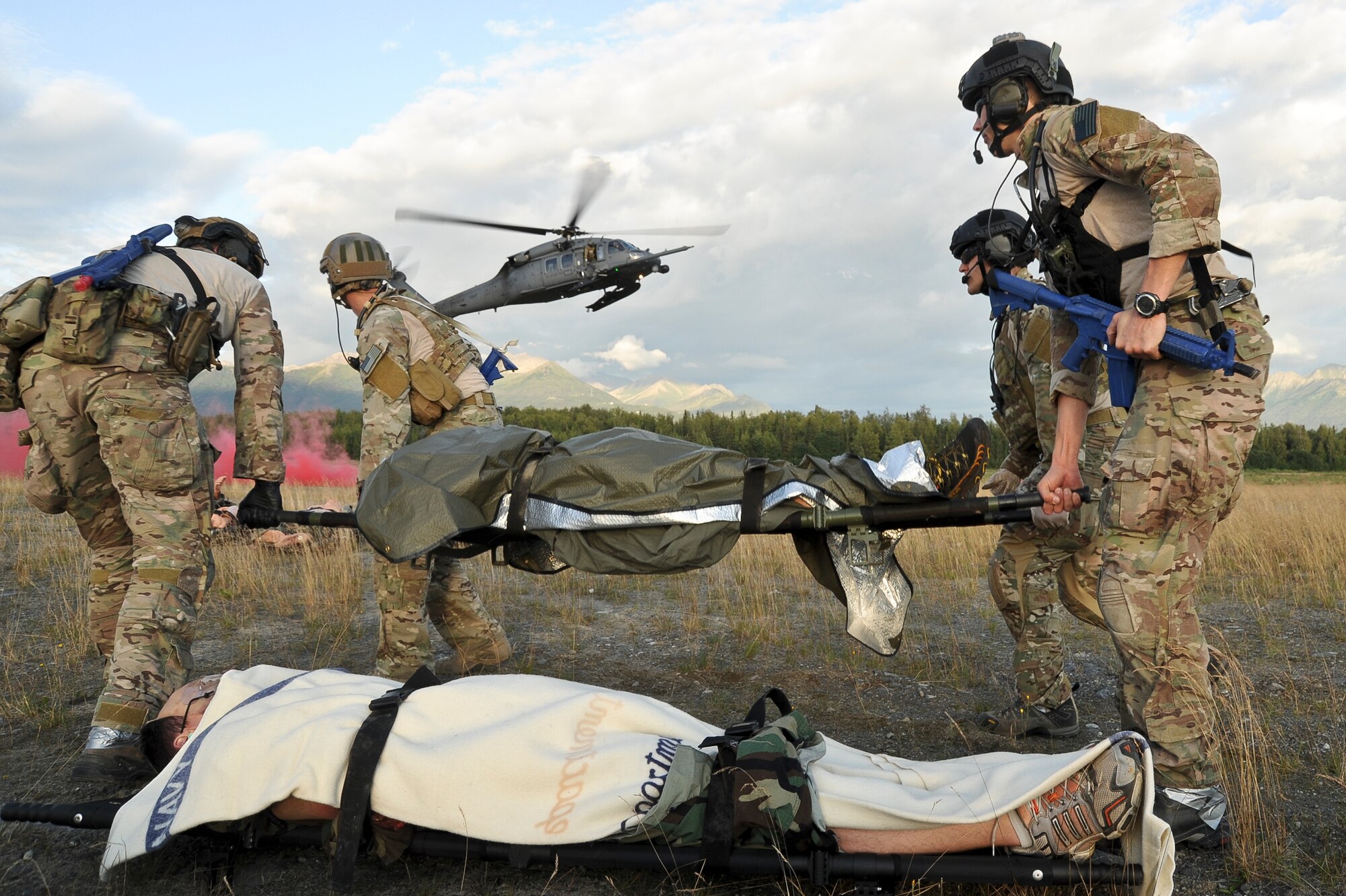 U.S. Air Force pararescuemen also known as PJ (para-jumper) from the, Alaska Air National Guard Joint Base Elmendorf-Richardson, Alaska,  and (Pararescue/Guardian Angels) from Davis-Monthan AFB Ariz.,  provide medical treatment to a simulated patients, while a 210th Rescue Squadron, HH-60G Pave Hawk helicopter hovers in the background July 30, 2014. The PJs are responsible for providing emergency and lifesaving services to military members and civilians in both peacetime and combat environments, they go behind enemy lines before anyone else to set on a drop zone/air field and help call in fire support.