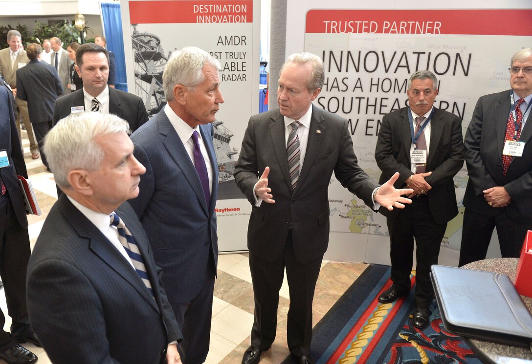 Defense Secretary Chuck Hagel, center, listens as a representative of Raytheon explains items in his company's exhibit booth during the Southeastern New England Defense Industry Alliance's Defense Innovation Days in Newport, R.I., Sept. 3, 2014.