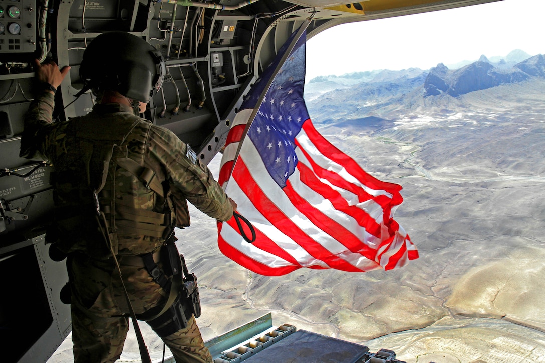 U.S. Army Sgt. Michael Misheff flies the American flag from the back of a CH-47 Chinook helicopter over southern Kandahar province, Afghanistan, Aug. 24, 2014. Pilots and crew chiefs fly American flags that are later presented with certificates to service members as part of aviation tradition. Misheff is a crew chief assigned to the 16th Combat Aviation Brigade.