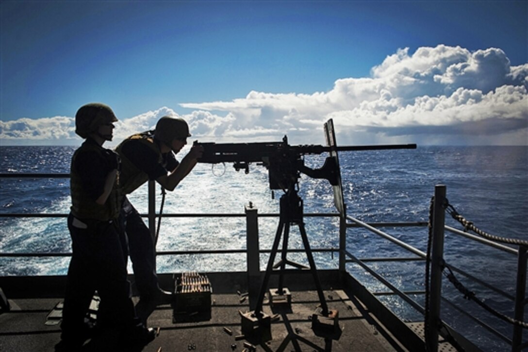 U.S. Navy Petty Officer 2nd Class Ashley Jebens, left, watches as Airman Joel Ochoa fires a machine gun from the fantail of the USS Carl Vinson in the Pacific Ocean, Aug. 29, 2014. The Carl Vinson is underway in the U.S. 3rd Fleet area of responsibility. 