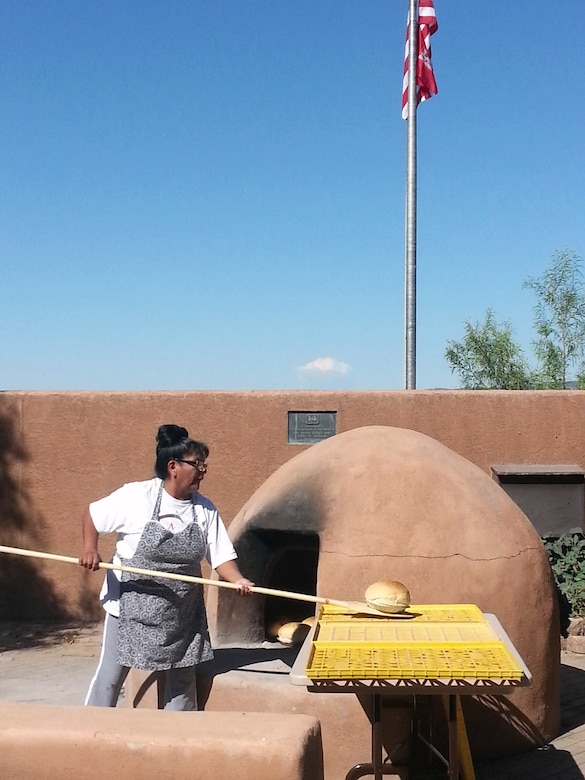 COCHITI LAKE, N.M., -- Cochiti Tribal member Marian Valdo takes baked bread out of the the “Kuush-Ku,” – the bread oven – located in the Visitor Center courtyard, Aug. 9, 2014. This was the first time the "Kuush-Ku" was used for its intended purpose. 