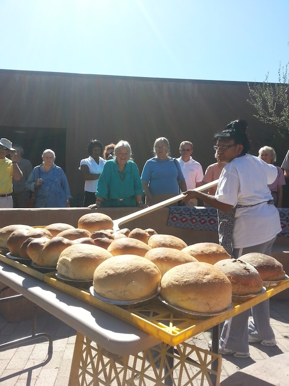 COCHITI LAKE, N.M., -- Attendees at the  Aug. 9, event watch as Marian Valdo brings bread out of the "Kuush-Ku" or bread oven, located in the Visitor Center Courtyard.  This was the first time the oven was used to bake bread.
