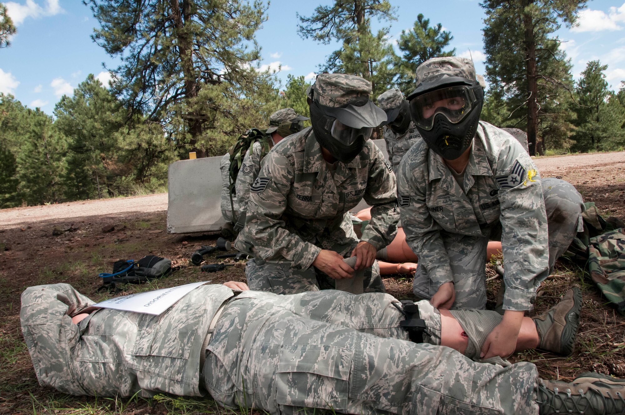 Tech. Sgt. Christine Yebra and Staff Sgt. Cory Zehner put their self-aid and buddy care skills to the test while keeping an eye out for enemy gun fire during the care-under-fire exercise. More than 70 Airmen from the 162nd Wing ventured up to the cool pines of Bellemont, Ariz. during a training exercise Aug. 11-15 at Camp Navajo Collective Training Center. (U.S. Air National Guard photo by 2nd Lt. Lacey Roberts)