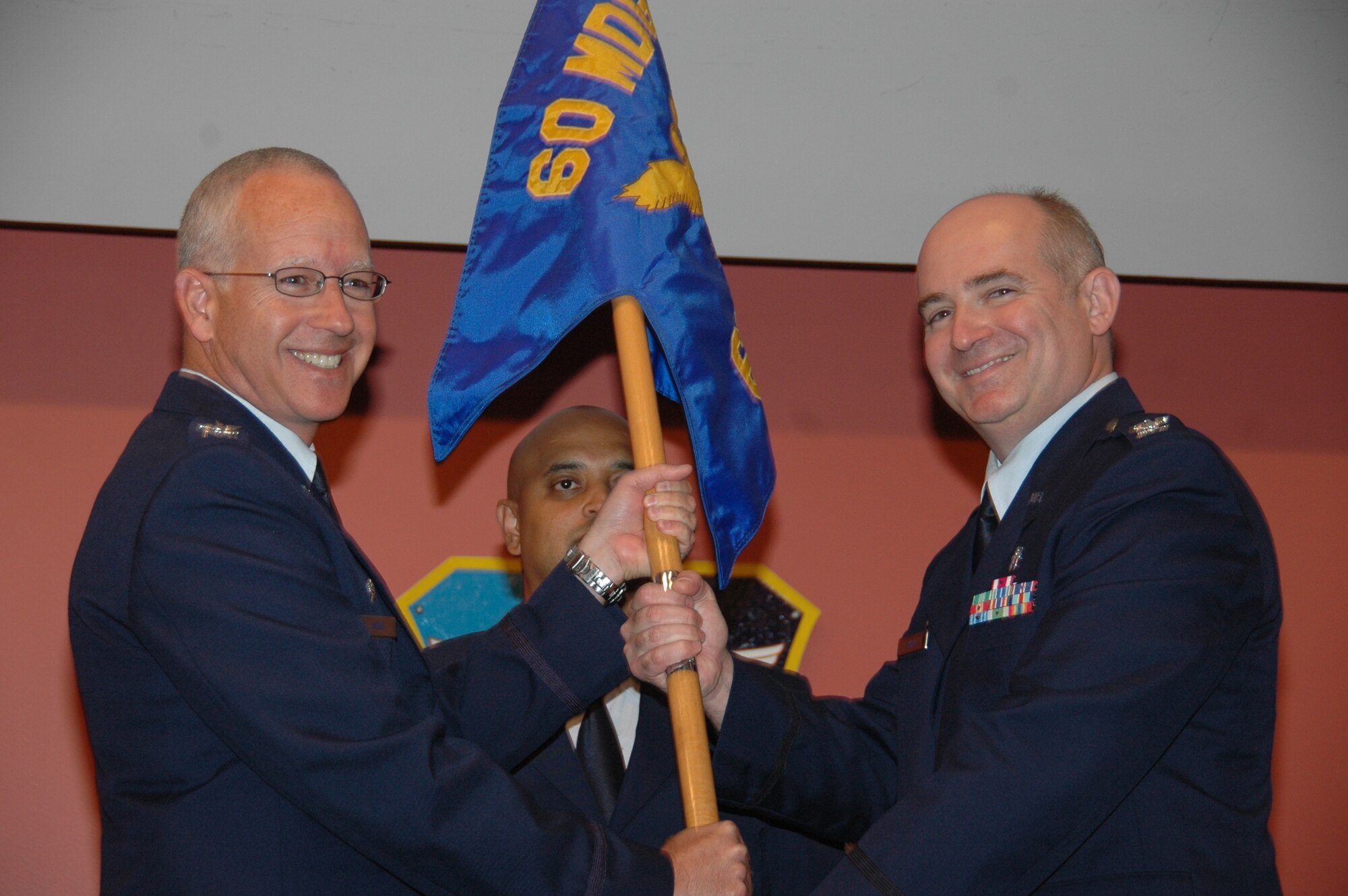 Col. (Dr.) Dave Simon (right), accepts the guidon from Col. (Dr.) Rawson Wood, 60th Medical Group commander during the 60th Surgical Operations Squadron change of command ceremony at David Grant USAF Medical Center.  During the ceremony, the squadron’s designation of 60 MSGS was officially switched to 60 SGCS to align with recent Air Force-level changes. (U.S. Air Force photo: Jim Spellman)