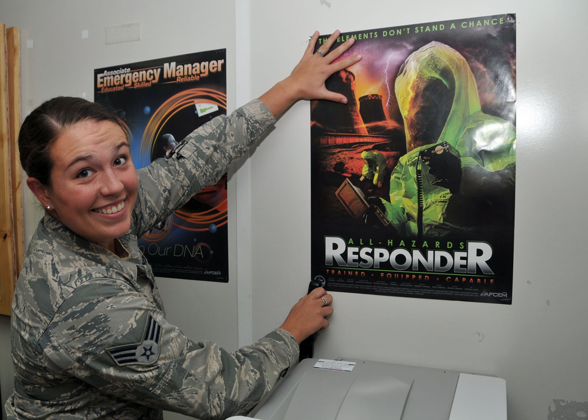 Air Force Senior Airman Rachel Riley places a poster on an office wall to inform base personnel of disaster preparedness issues at the 380th Air Expeditionary Wing at an undisclosed location in Southwest Asia Aug. 27, 2014. (U.S. Air National Guard photo by Senior Master Sgt. Eric Peterson/Released)