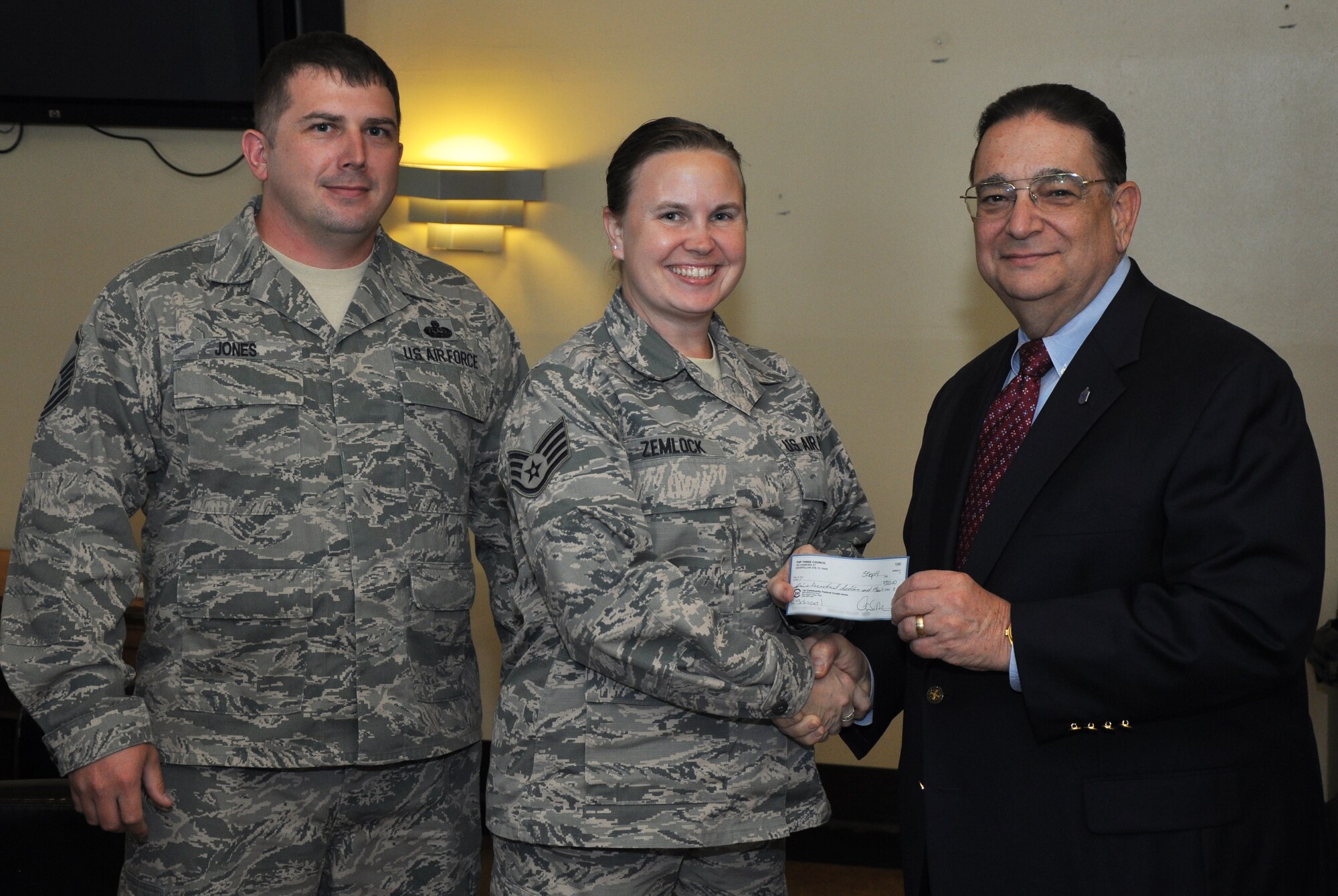 GOODFELLOW AIR FORCE BASE, Texas – Mike Mitchell, Top 3 scholarship funder, and Master Sgt. Andrew B. Jones, 17th Training Support Squadron Training Systems Support flight chief present Staff Sgt. Kara S. Zemlock, 17th Training Group student out processing NCO in charge, with a $500 check from the Top 3 at the Event Center Sept. 5. Zemlock plans to use her scholarship toward her master’s degree. (U.S. Air Force photo illustration/ Senior Airman Joshua Edwards)