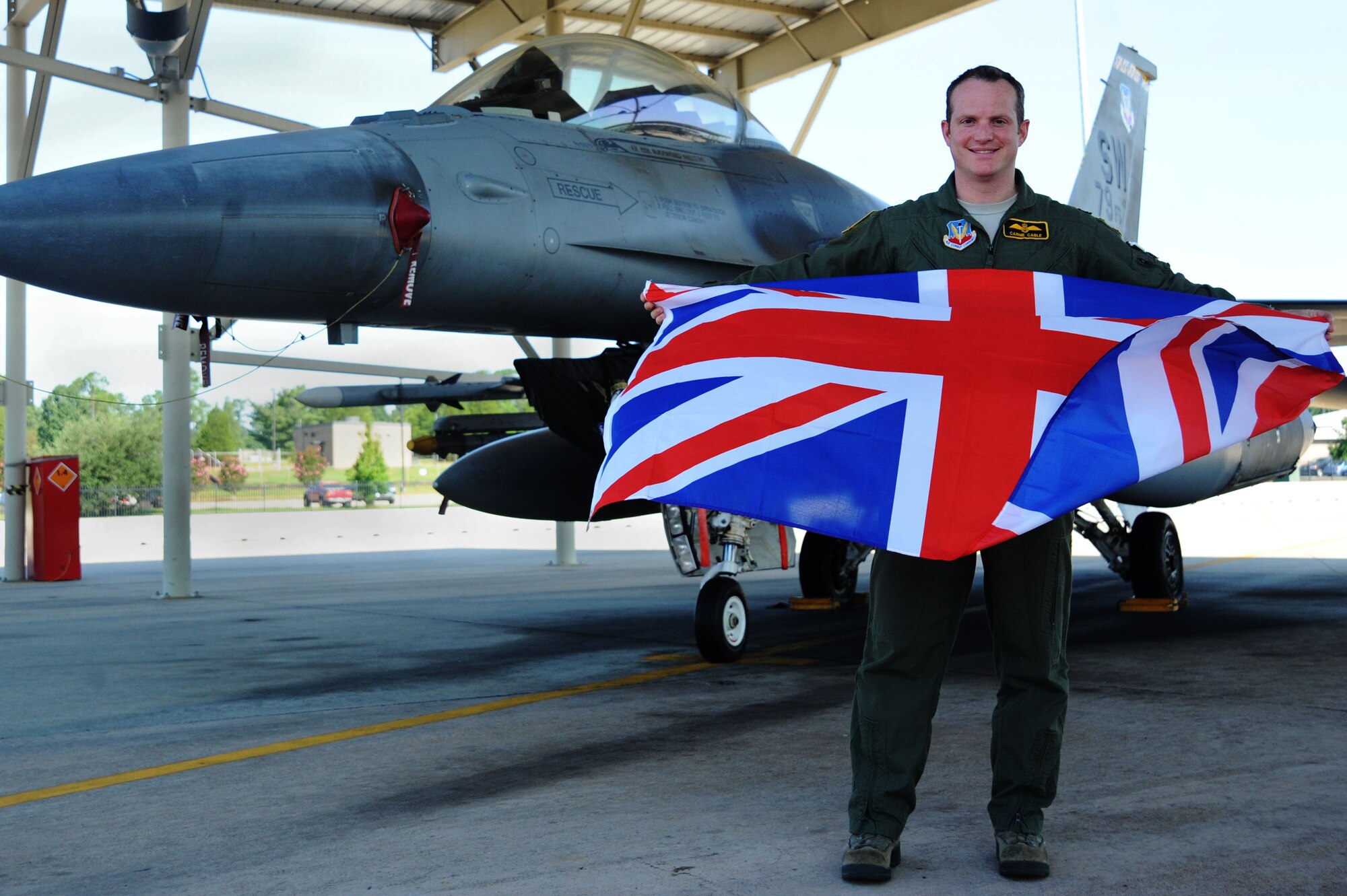 Royal Air Force Flight Lieutenant Benjamin Cable, 79th Fighter Squadron assistant director of operations, displays the United Kingdom flag in front of an F-16CM Fighting Falcon at Shaw Air Force Base, S.C., Aug. 21, 2014. Cable, a Brighton, United Kingdom native, has been on active duty status for 13 years, in which time he has been on four deployments. (U.S. Air Force photo by Airman 1st Class Michael Cossaboom/Released)