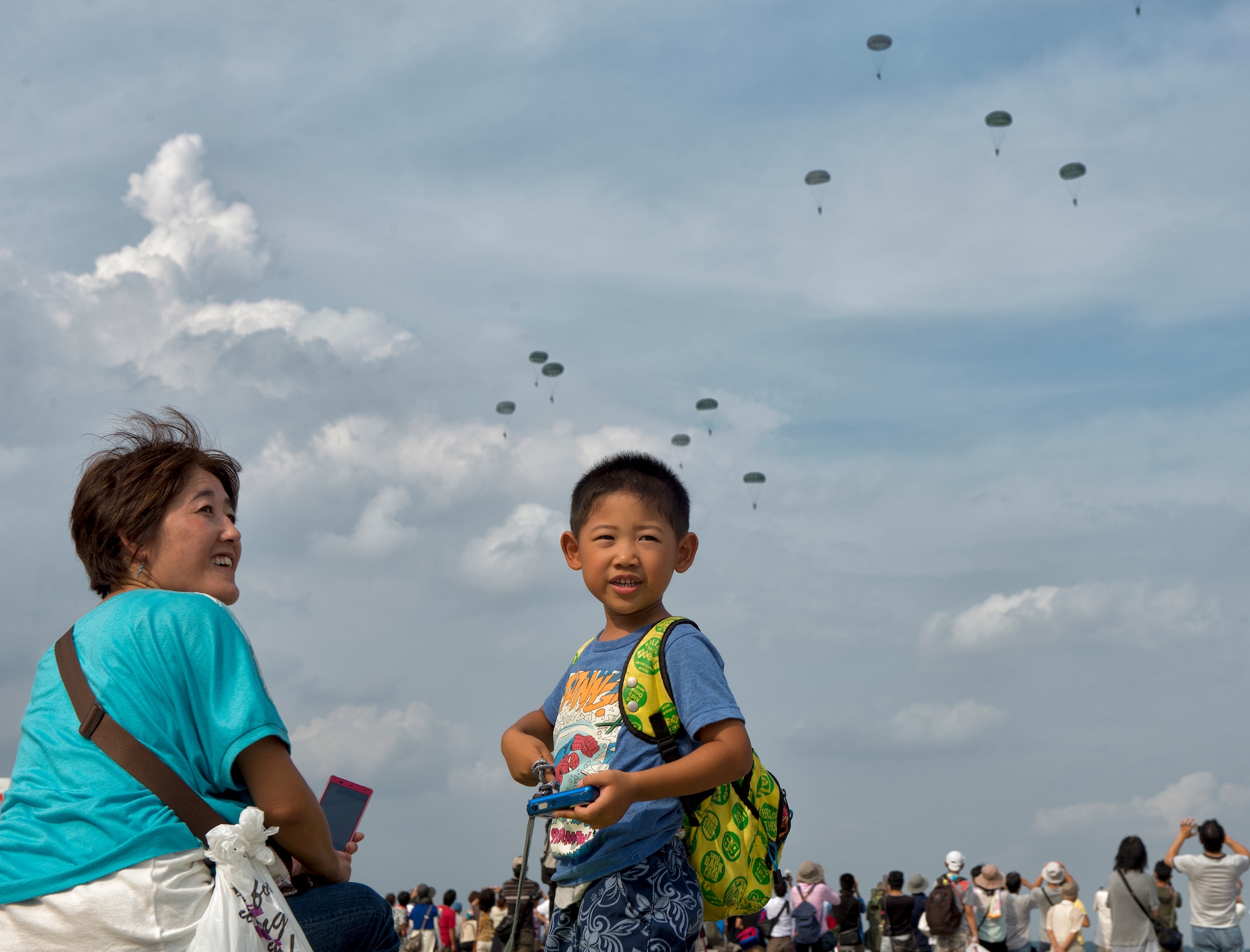 A local boy and mother watches an airdrop demonstration performed by U.S. Soliders from the 1st Battalion, 1st Special Forces Group (Airborne) at Yokota Air Base, Japan, during the Japanese-American Friendship Festival Sept. 6, 2014. Yokota welcomed approximately 148,000 visitors during the two-day festival. (U.S. Air Force photo by Osakabe Yasuo/Released)   