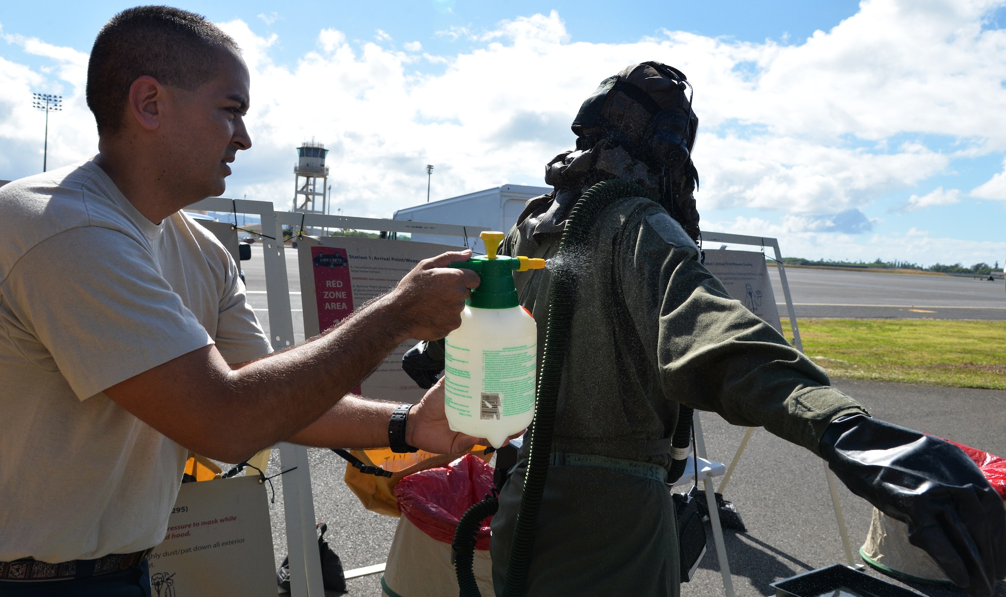 Tech. Sgt. Ryan Hunt, 15th Operations Support Squadron, sprays simulated decontamination solution on Airman 1st Class Rebekah McCormack, 96th Air Refueling Squadron, during an emergency preparedness training event Sept. 5, 2014, at Joint Base Pearl Harbor-Hickam, Hawaii. McCormack and other 96th ARS members participated in the chemical, biological, radiological and nuclear training that ensures they are prepared to operate in a contaminated environment. Hunt and his team from the 15th OSS and 199th Fighter Squadron aircrew flight equipment sections manned decontamination stations as part of the Aircrew Contamination Control Area, which aircrew members had to pass through to conclude the training. Note: In a real-world CBRN environment, the AFE crew would also be in individual protective equipment. (U.S. Air Force photo by Staff Sgt. Alexander Martinez)