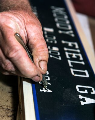 John Fischbach Sr., 23d Force Support Squadron recreation aide, lays a stencil on a block of wood Aug. 8, 2014, at Moody Air Force Base, Ga. Fischbach uses this stencil and ones like it to make the Moody Field, Ga., signs that are one of the typical going-away gifts for people leaving the base. (U.S. Air Force photo by Senior Airman Jarrod Grammel/Released)
