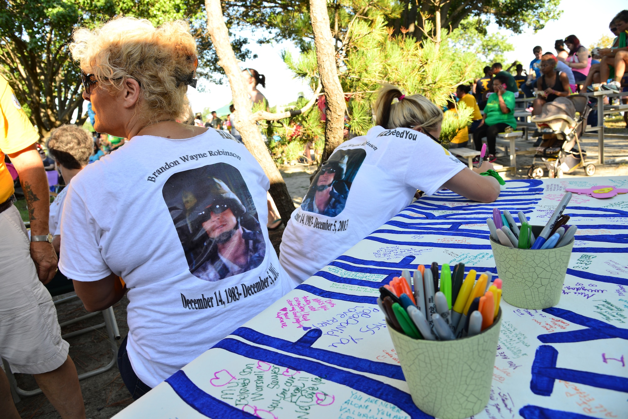 The family members of U.S. Marine Corps veteran and suicide victim Brandon Wayne Robinson celebrate his life by wearing shirts adorned with his photo and by writing personal messages on a banner before the start of the Out of Darkness community walk in Virginia Beach, Va., Sept. 6, 2014. In addition to wearing memorial shirts, several walk participants wore ribbons of various colors which symbolized their connection to suicide. (U.S. Air Force photo by Senior Airman Aubrey White/Released)