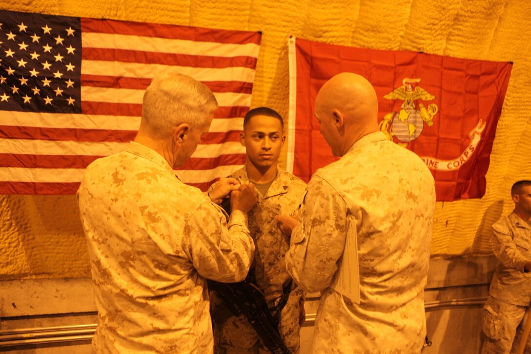 General James F. Amos, left, the 35th Commandant of the Marine Corps, and Sgt. Maj. Micheal Barrett, right, the 17th Sergeant Major of the Marine Corps, pin corporal chevrons on Cpl. Miguel Mercedes, an ammunition technician specialist with Redeployment and Retrograde in support of Reset and Reconstitution Operations Group, during his meritorious promotion ceremony aboard Camp Leatherneck, Afghanistan, Sept. 6, 2014. General Amos meritoriously promoted Mercedes, a native of Bronx, New York, to the rank of corporal during his final visit to Helmand province.