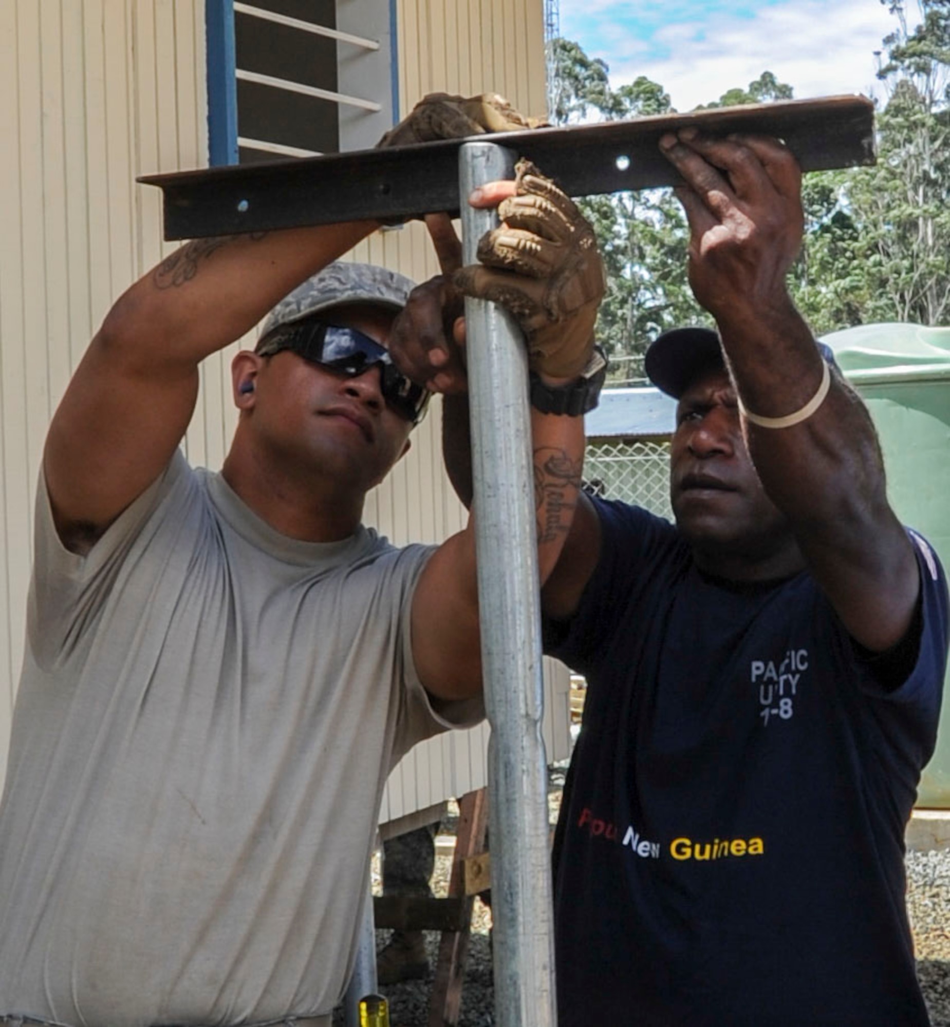 Senior Airman Malcolm Yin, 154th CES emergency management journeyman, twists a screw while Petrus Buka, a day laborer from the local community, holds a pole in place at Togoba Secondary School in Mount Hagen, Papua New Guinea, Sept. 8, 2014. Yin and Buka are constructing a clothesline, which will be used by residents of the newly constructed female dormitories, as part of Pacific Unity 14-8. Pacific Unity helps cultivate common bonds and foster goodwill between the U.S. and regional nations through multilateral humanitarian assistance and civil military operations. (U.S. Air Force photo by Tech. Sgt. Terri Paden/Released)