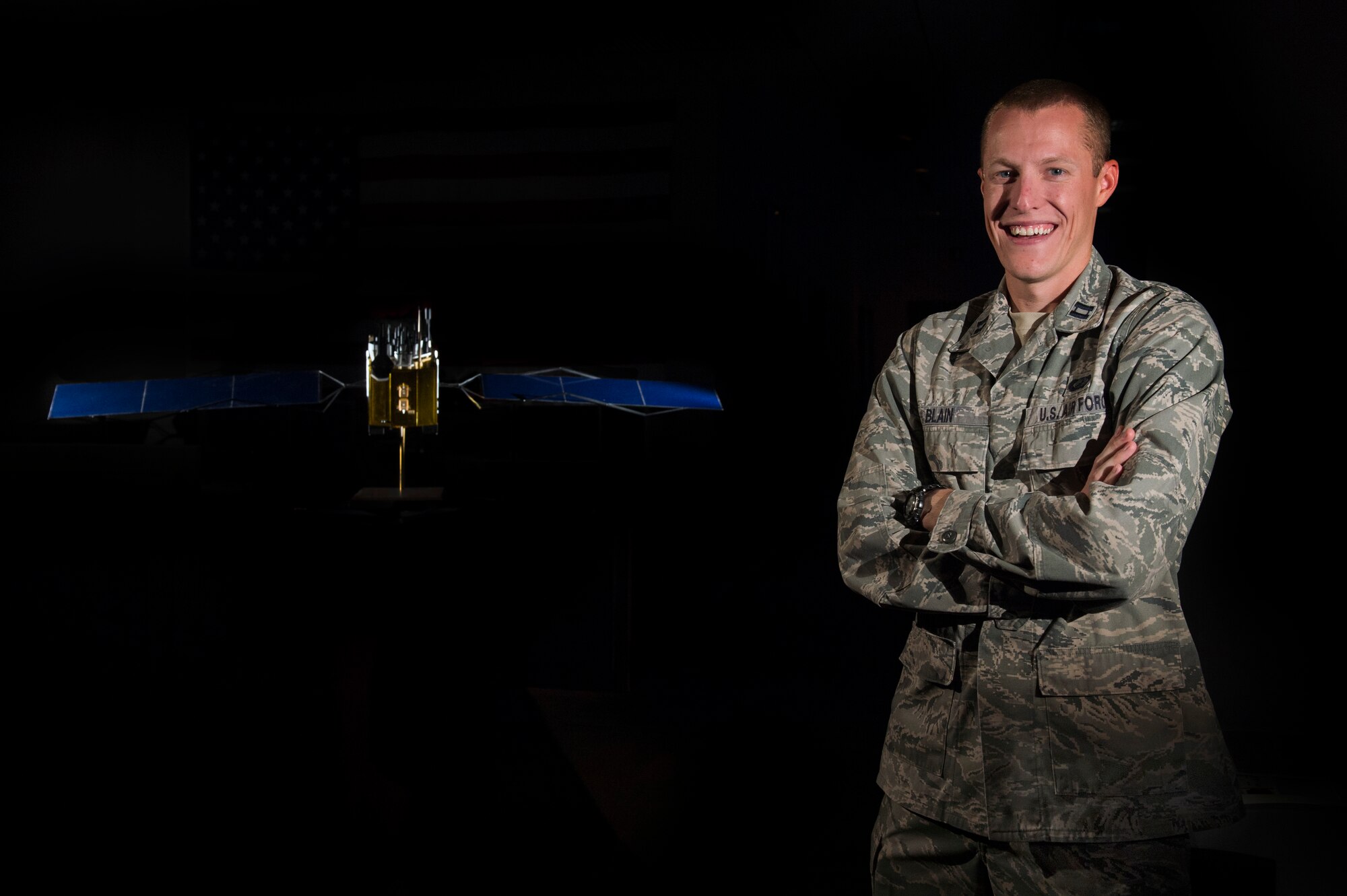 Capt. Aaron Blain, 2nd Space Operations Squadron chief of navigation analyst payload, stands in front of a model of a Block IIF GPS-satellite on Schriever Air Force Base, Colo., Sept. 4, 2014. Blain maintains communications with satellites to optimize signals that serve 3.5 billion daily users. (U.S. Air Force photo/Airman 1st Class Krystal Ardrey)