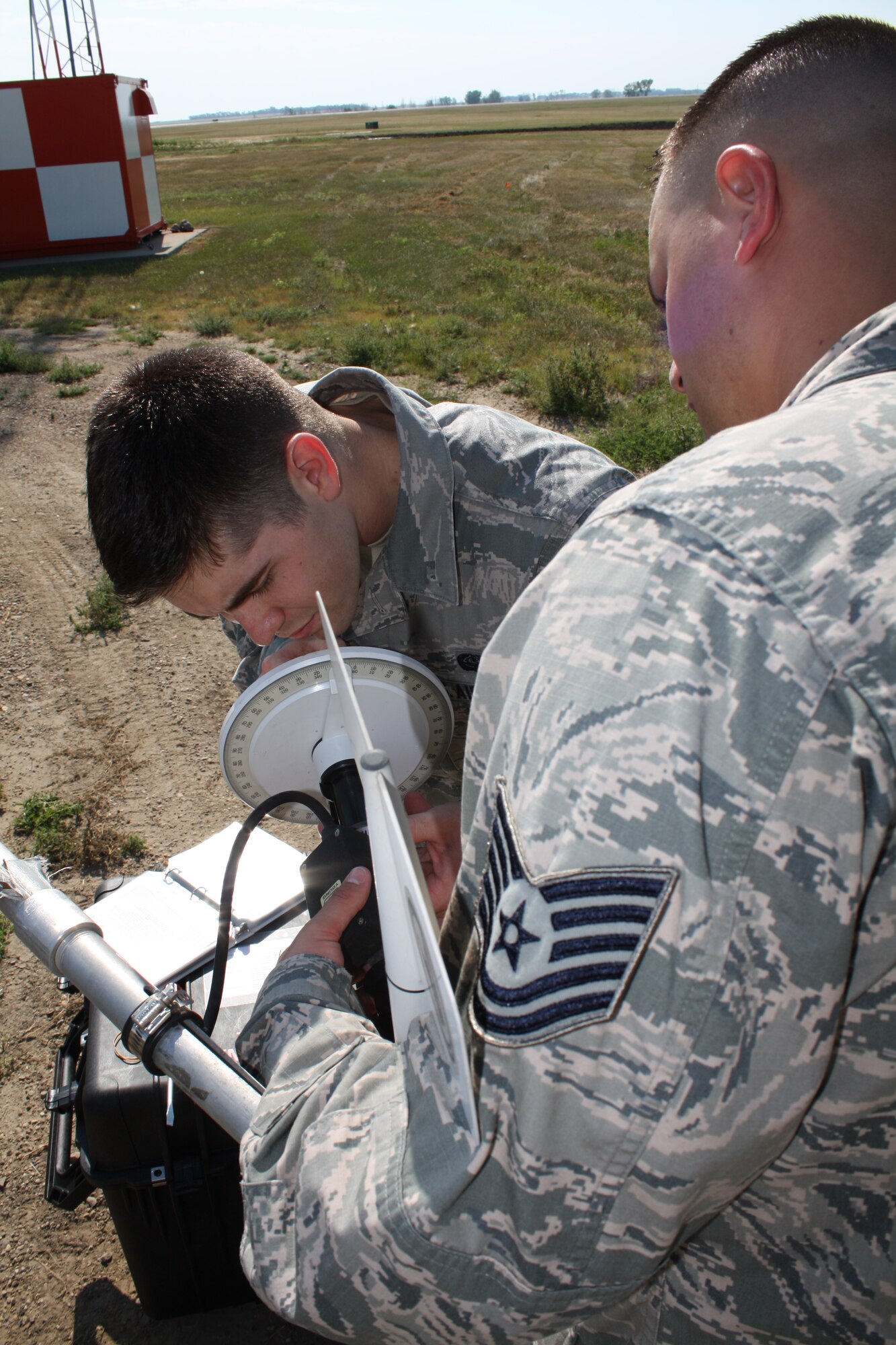 Tech. Sgt. Joshua C. Stewart (right), 5th Communications Squadron air traffic control airfield landing systems section chief, and Airman 1st Class Jon R. Marsh, 5th CS airfield systems apprentice, set up test equipment to verify the accuracy of a wind monitor on Minot Air Force Base, Aug. 12. The monitor senses both horizontal wind speed and direction, helping weather forecasters assess current flying conditions. (U.S. Air Force photo/Capt. Jeff M. Nagan)