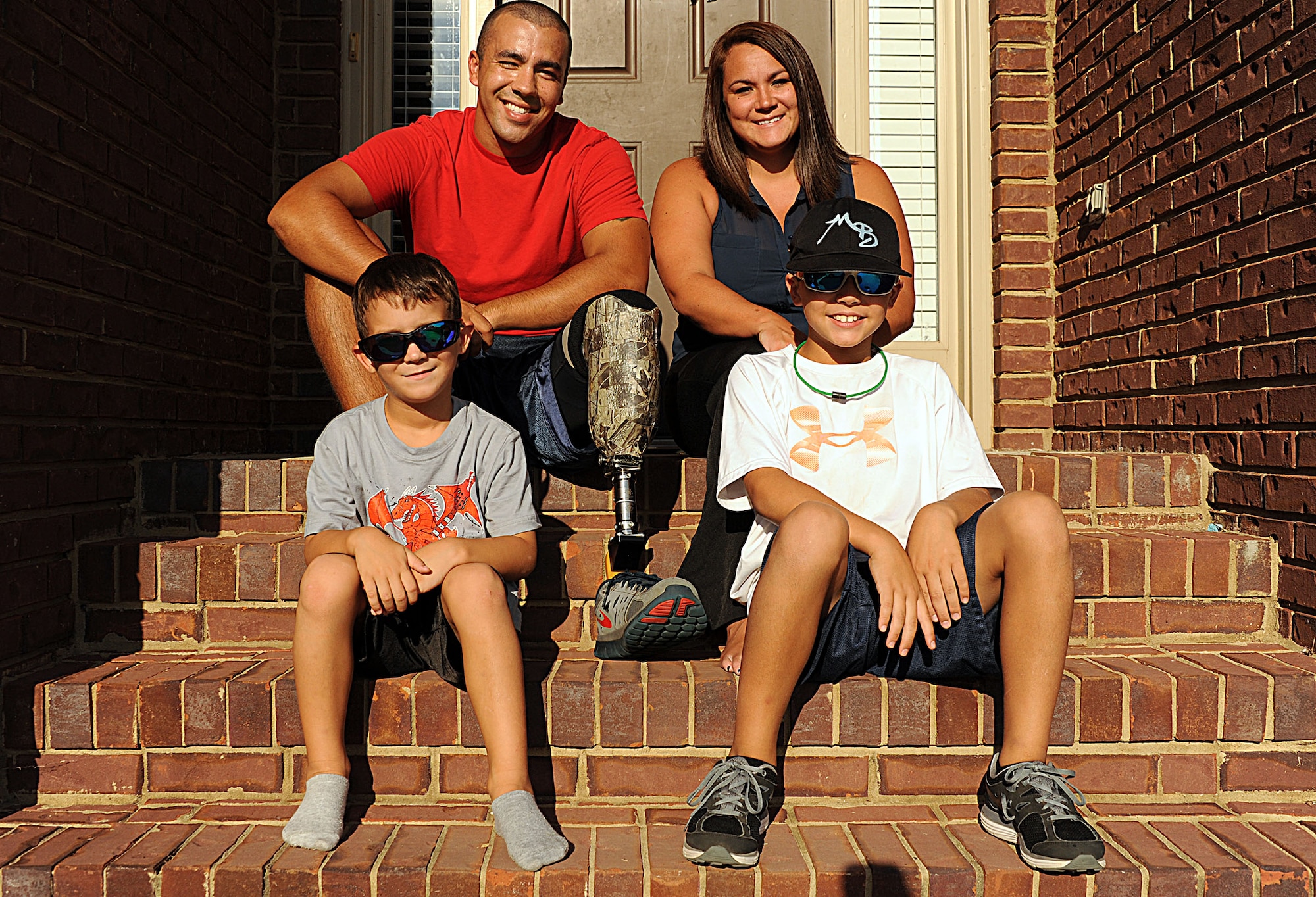 Staff Sgt. Rey Edenfield, a Maxwell Air Force Base air traffic controller, poses with his wife, Amy, and their two sons, Grayson (left) and Dawson (right), on the front porch of their home Aug. 28. This picture was taken almost a year after Edenfield was involved in a motorcycle accident that resulted in his left leg being amputated six inches below the knee. (U.S. Air Force photo by Staff Sgt. Erica Picariello))