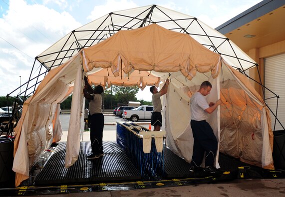 U.S. Air Force Airmen from the 7th Medical Group raise an articulating frame shelter as part of in-place patient decontamination training Sept. 4, 2014, at Dyess Air Force Base, Texas. During this training the decontamination facility had to be mission capable in 15 minutes and fully functional within 20 minutes of emergency notification. (U.S. Air Force photo by Senior Airman Kia Atkins/Released)
