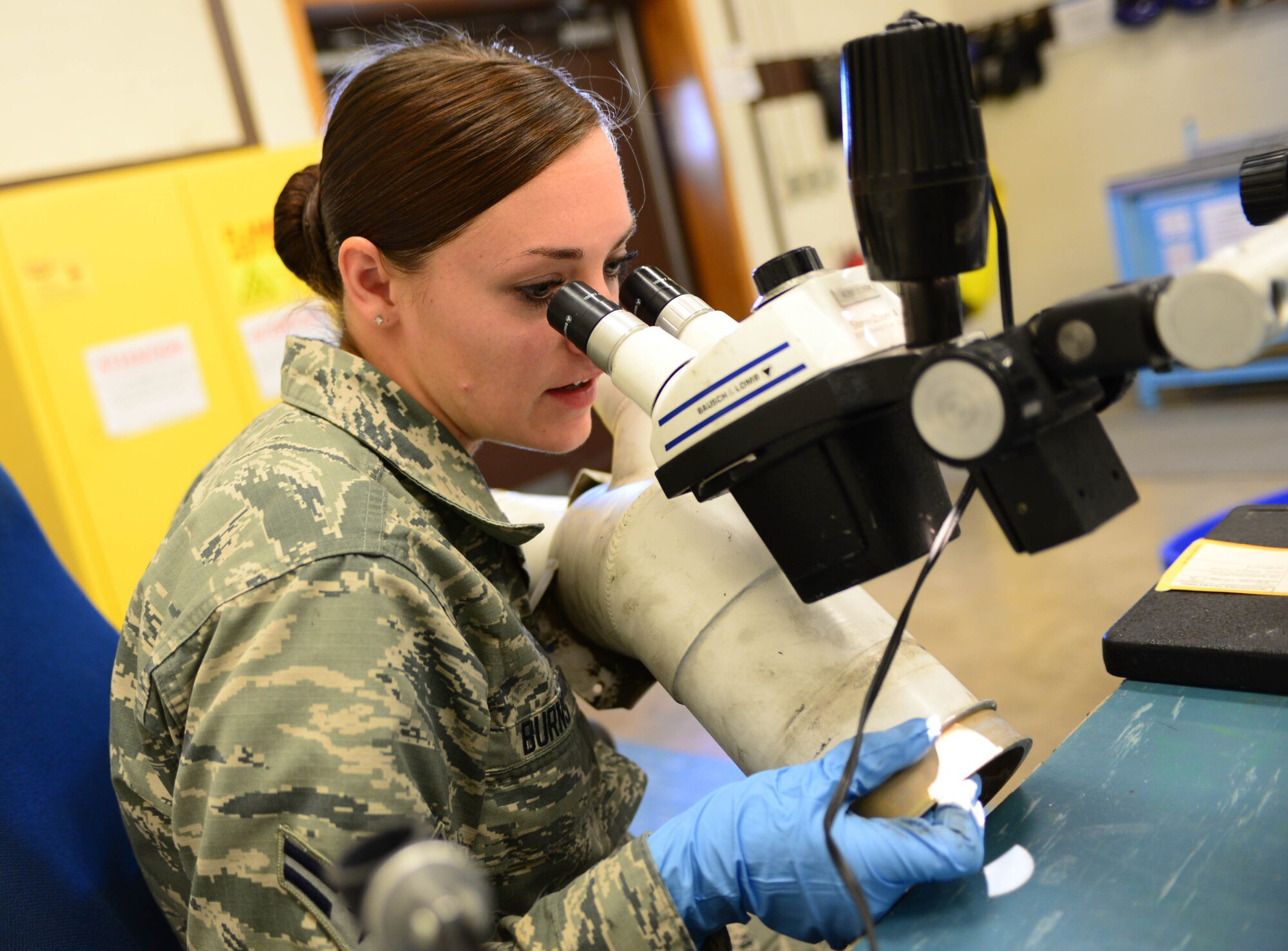 Airman 1st Class Amber Burns, 28th Maintenance Squadron non-destructive inspection apprentice, examines a fuel manifold tube under a stereo-zoom microscope during an inspection at Ellsworth Air Force Base, S.D., Sept. 8, 2014. NDI is the examination of aerospace weapon systems components and support equipment for structural integrity using non-destructive inspection methods and fluid analysis. (U.S. Air Force photo by Senior Airman Zachary Hada/Released)
