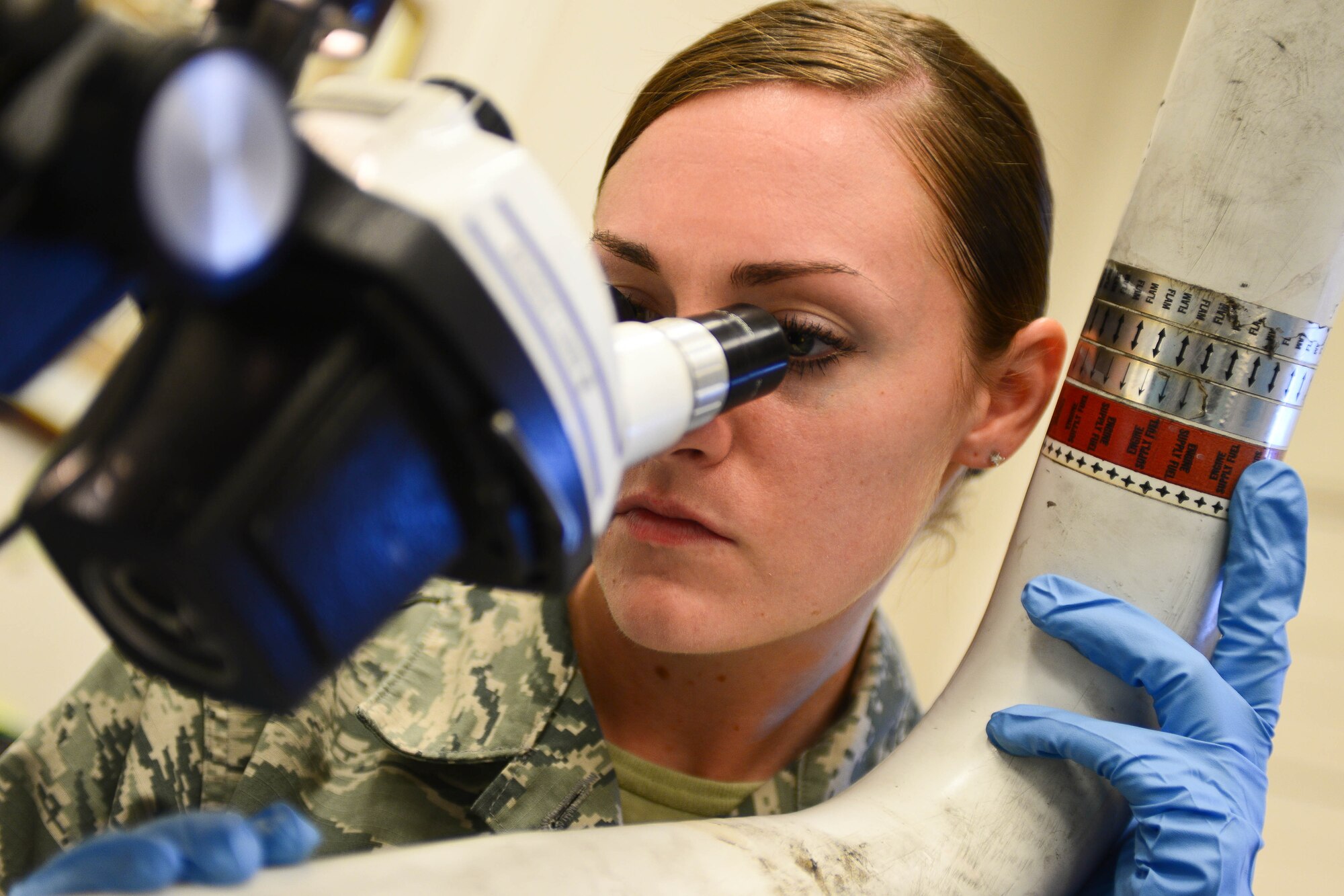 Airman 1st Class Amber Burns, 28th Maintenance Squadron non-destructive inspection apprentice, examines a fuel manifold tube under a stereo-zoom microscope during an inspection at Ellsworth Air Force Base, S.D., Sept. 8, 2014. The inspection enhances the capability to identify imperfections of aircraft parts if any are found, the part is sent to shops on base where they can be repaired or replaced. (U.S. Air Force photo by Senior Airman Zachary Hada/Released)