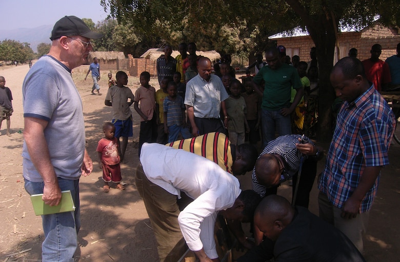 Dave Ray, chief of geotechnical sciences branch, Omaha District USACE shares a western piece of engineering equipment with the local TANROADS engineers, while villagers look on. 