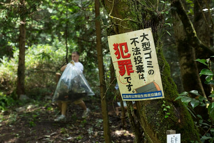Pfc. Brandon Messina, a volunteer from Marine Corps Air Station Iwakuni, Japan, carries a bag of trash past a “no littering” sign during a river cleanup, sponsored by the Single Marine Program, in Asakita-ku, Hiroshima, Sept. 5, 2014. This was the first cleanup the SMP conducted in Hiroshima recently.