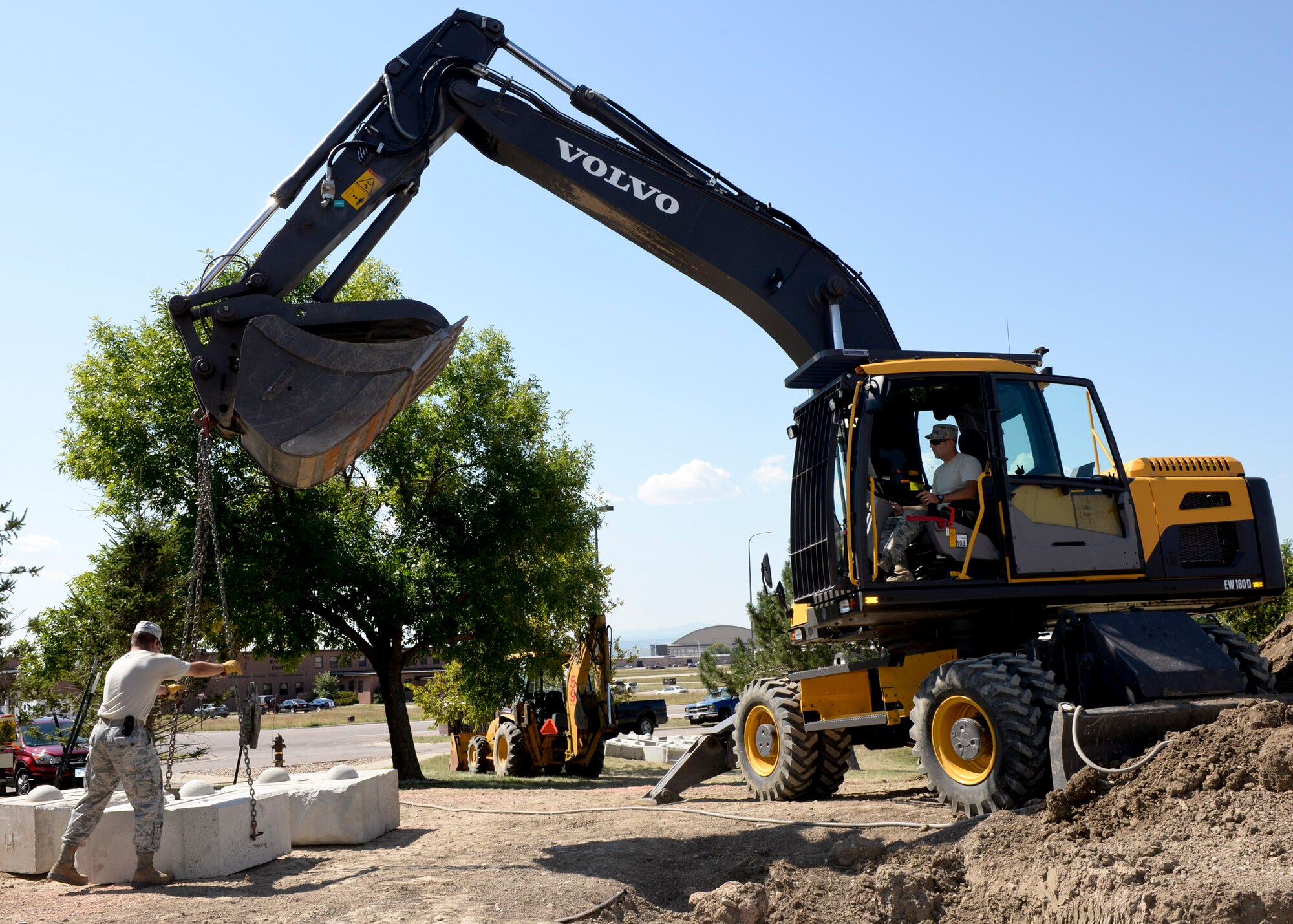 Tech. Sgt. James Banik, 28th Civil Engineer Squadron heavy equipment technician, lifts 1,600 –pound blocks of cement using a wheeled excavator during the construction of a retaining wall outside the 28th Bomb Wing Headquarters building at Ellsworth Air Force Base, S.D., Sept. 8, 2014. When completed the wall will stand over seven feet tall and protect the building from rain damage. (U.S. Air Force photo by Senior Airman Anania Tekurio/Released)
