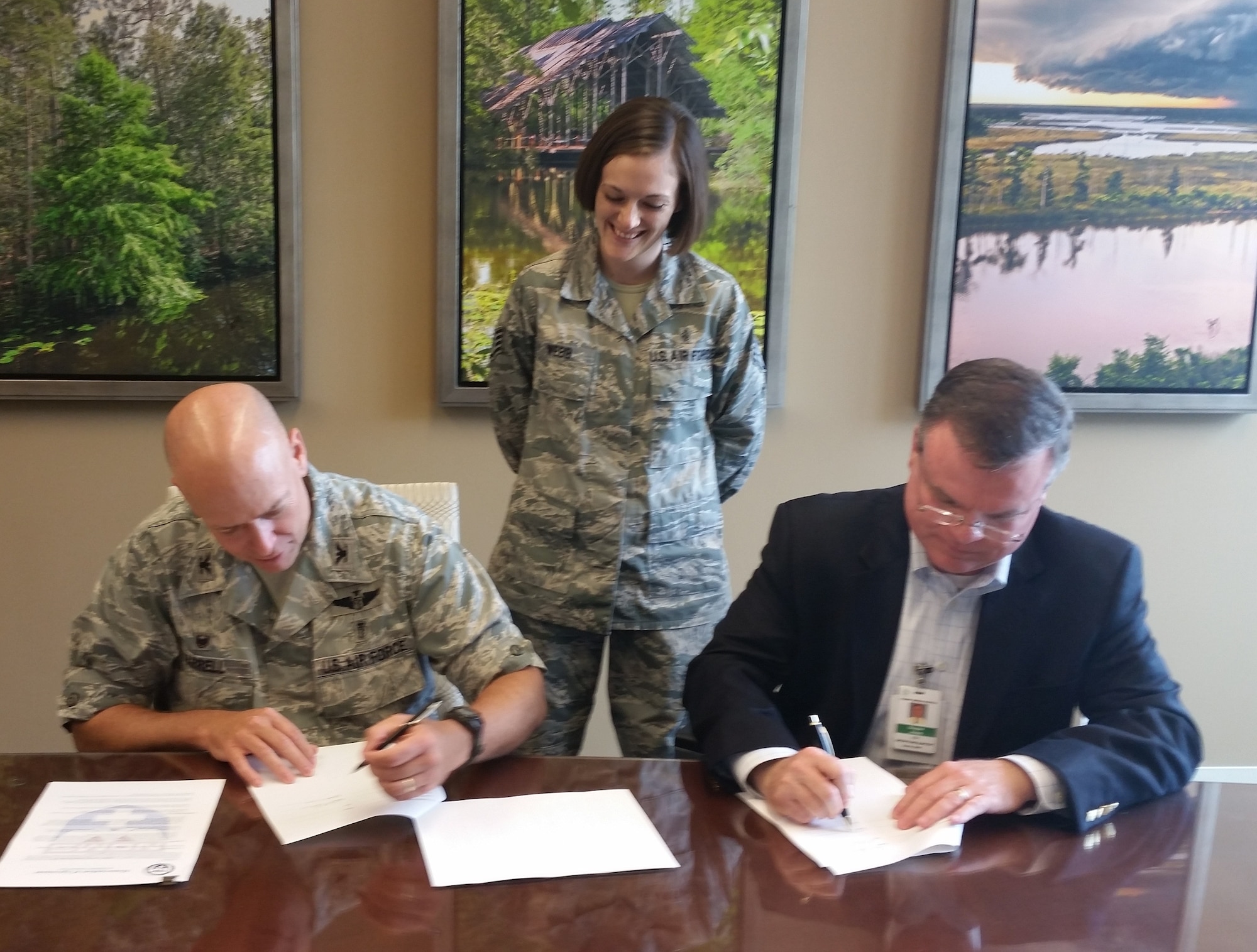 Staff Sgt. Hana Webb, National Disaster Medical System FCC area coordinator, watches Col. (Dr.) Tom Harrell, 81st Medical Group commander, left, and Douglas Jones, Forrest General Health System chief operating officer, sign an agreement Aug. 27 making the Picayune, Miss., medical facility Keesler Medical Center’s 25th partner hospital within the NDMS.  (Courtesy photo by Maj. Marlon Muthuveeran)
