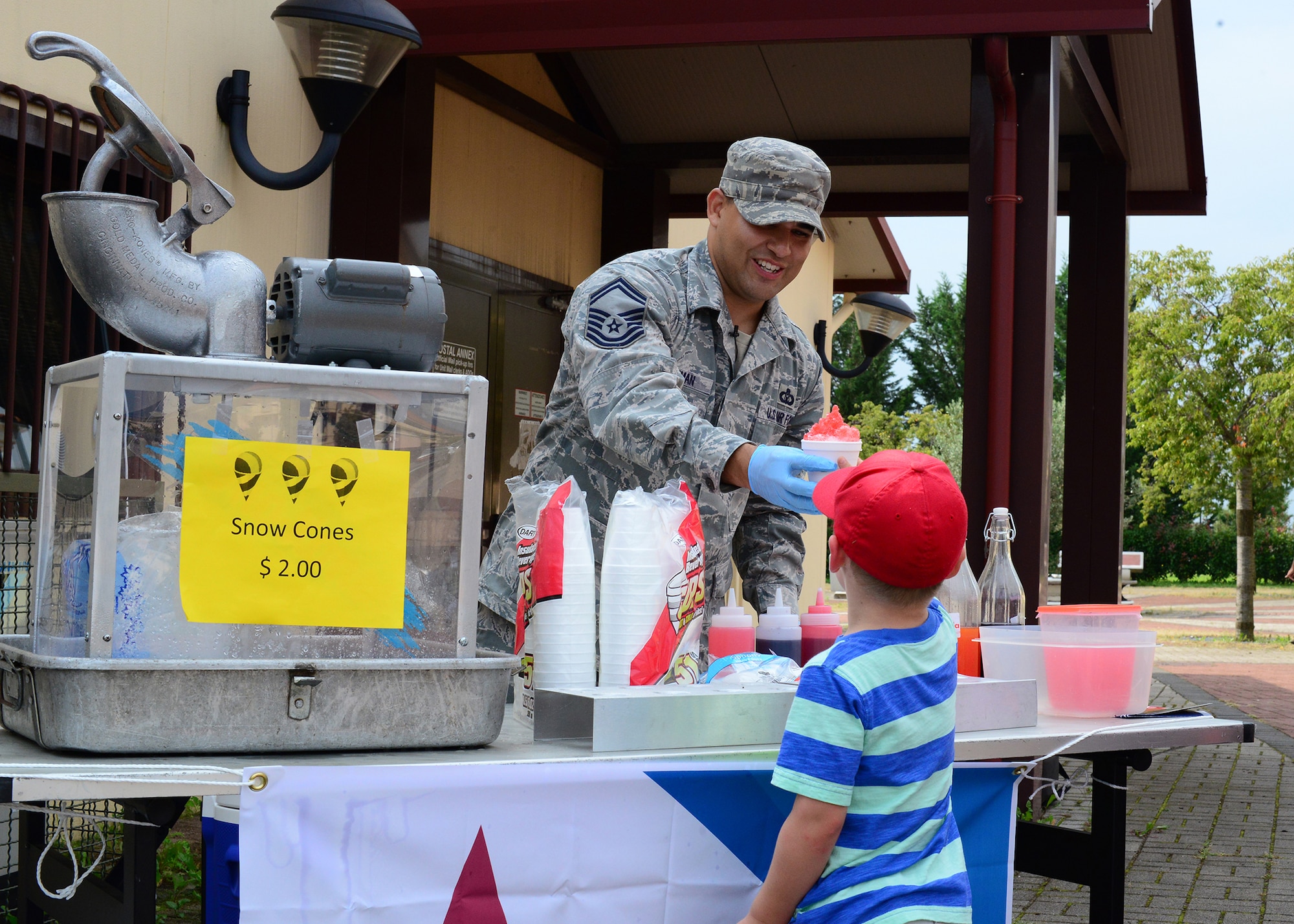 Senior Master Sgt. Bobby Hickman gives a snow cone to a child during a Combined Federal Campaign Overseas fundraising event, Sept. 4, 2014, at Aviano Air Base, Italy. The 31st Fighter Wing kicked off the CFC-O with a burger-burn and information booth near the Exchange, inviting guests to share a meal and browse through a catalogue of various charities. Hickman is assigned to the 31st Operations Support Squadron and one of this year’s CFC-O Project Officers. (U.S. Air Force photo/Staff Sgt. Jessica Hines)