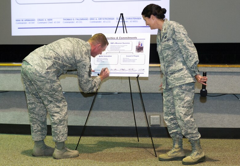Brig. Gen. Nina Armagno, 45th Space Wing commander, looks on as Chief Master Sgt. Craig Neri, 45th SW command chief, adds his signature to the group commander’s new priorities and commitments poster during the Commander’s Call, Sept. 5, 2014, at Patrick Air Force Base, Fla. The vision and mission statements were changed only slightly, but the priorities and commitments were revised to better reflect where we are, where we want to go, what we already do well, and where we need work. (U.S. Air Force photo/Cory Long) (Released)