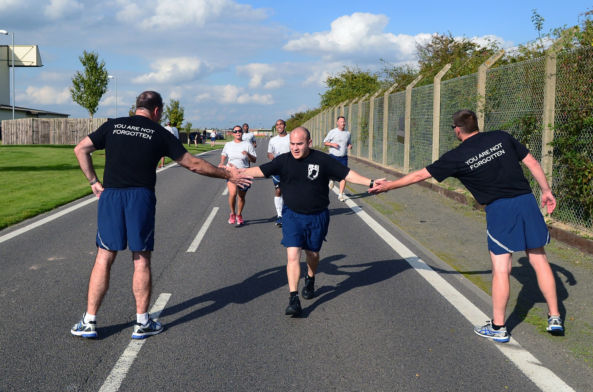 U.S. Air Force Col. Kenneth T. Bibb Jr., left, 100th Air Refueling Wing commander, and U.S. Air Force Chief Master Sergeant Tracy Jones, far right, 100th ARW command chief, high-five Team Mildenhall members as they finish the wing 5 km run in honor of Prisoner of War/Missing in Action Week of Remembrance Sept. 12, 2014, on RAF Mildenhall, England. Service members, civilians and their families participated in the 5 km run. (U.S. Air Force photo/Airman 1st Class Jonathan Light/Released)