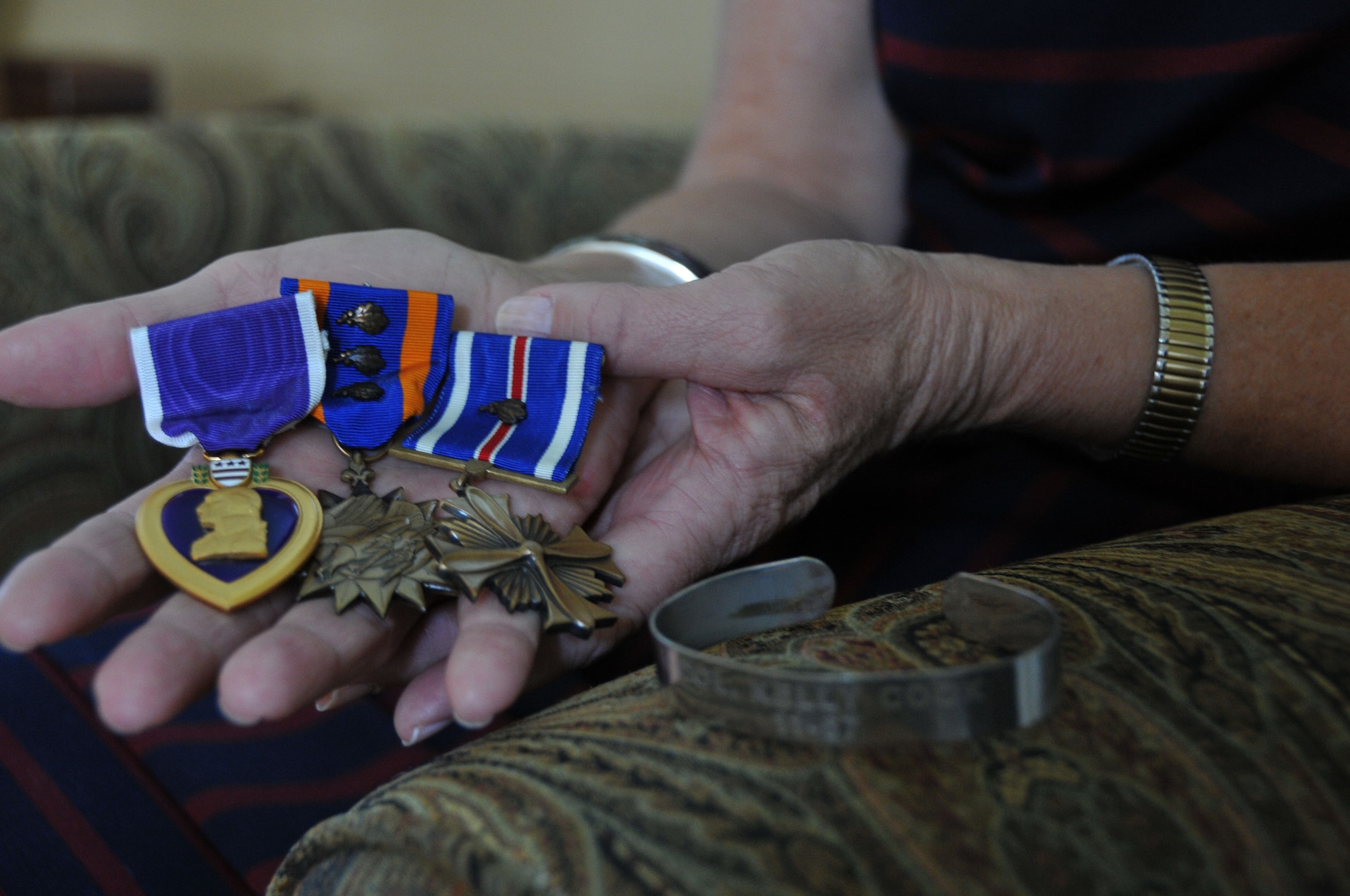 Maureen Kozak holds her father’s medals and displays a Prisoner of War Missing in Action bracelet bearing his name. Col. Kelly F. Cook was a fighter pilot who was listed as MIA in Vietnam and was later declared killed in action, body not recovered. Cook’s medals include a Purple Heart, two Distinguished Flying Crosses and four Air Medals. Maureen has corresponded with several supporters across the nation who have worn a POW/MIA bracelet with her father’s name on it, including a family she sends a Christmas card to every year. Maureen wore her bracelet as a teenager through adulthood until it broke; it’s now stored for safekeeping. (U.S. Air Force photo/Staff Sgt. Mercedes Crossland)