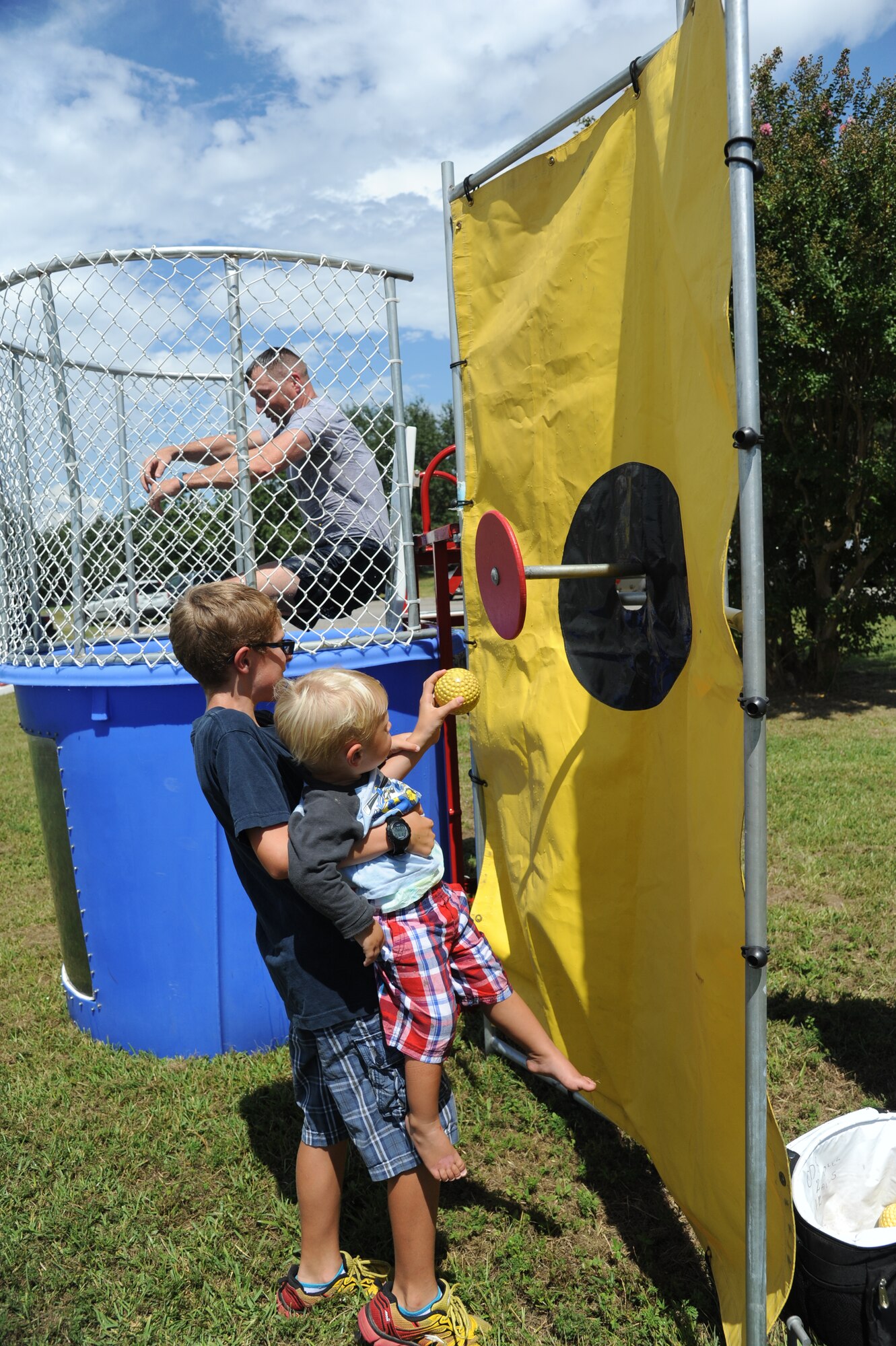 The sons of Lt. Col. James Coughlin, 85th Engineering Installation Squadron commander, presses the dunking booth target, dropping Brig. Gen. Patrick Higby, 81st Training Wing commander, into the booth during the Fisher House Fundraiser paintball tournament Sept. 12, 2014, at the paintball complex, Keesler Air Force Base, Miss.  The event also included food and games. (U.S. Air Force photo by Kemberly Groue)
