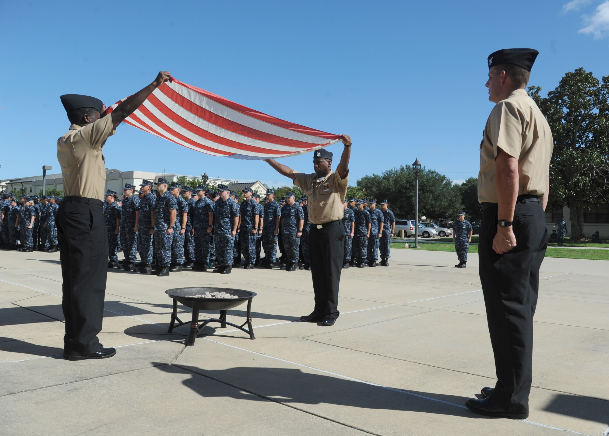 Petty Officers 1st Class Quintron Perry and Sedric Jones, Center for Naval Aviation Technical Training Unit Keesler, prepare to burn a worn U.S. flag, which is the proper procedure for retiring a U.S. Flag, as Petty Officer 1st Class Nathan Bizzle stands by during a remembrance ceremony Sept. 11, 2014, Keesler Air Force Base, Miss.  The ceremony also honored those who lost their lives during the 9/11 attacks. (U.S. Air Force photo by Kemberly Groue)