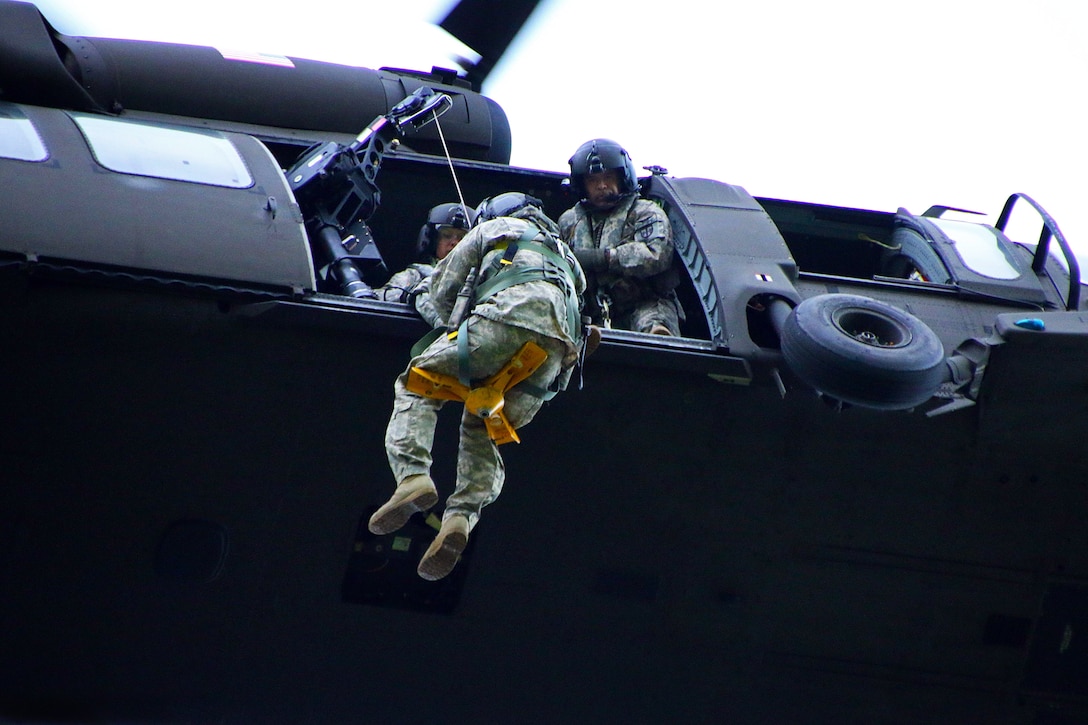 Army crew chiefs inside a UH60 Black Hawk helicopter hoist up a
