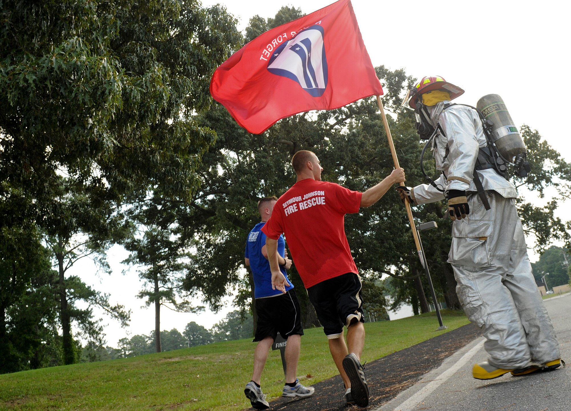 Airmen participating in the 24-hour 9/11 Remembrance Run pass the 9/11 memorial flag to two firefighters in full gear from the 4th Civil Engineer Squadron at Seymour Johnson Air Force Base, North Carolina, Sep. 11. Members of Team Seymour ran continuously with the 9/11 memorial flag for 24 hours. The run began at 9 a.m. when the fire department’s youngest firefighter left the firehouse carrying the flag and ended when the oldest, Sean Quinby, 4th CES fire chief, returned it 24 hours later. Participants racked up a combined total of 1,397 miles ran. (U.S. Air Force photo/Airman 1st Class Aaron Jenne)