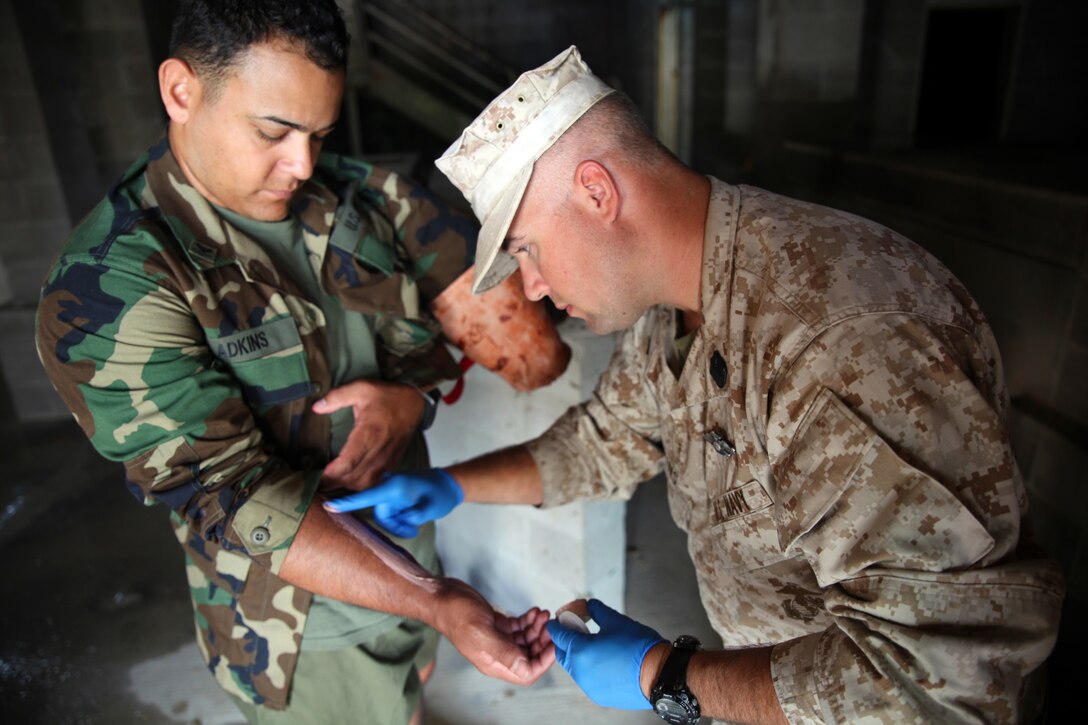 Petty Officer 2nd Class Derrick A. Adkins (back), battalion corpsman for 2nd Intelligence Battalion, II Marine Expeditionary Force, and a native of Chattanooga, Tenn., applies a simulated trauma to the arm of Sgt. Erick J. Velazquez, a geospatial intelligence analyst for 2nd Intel Bn, II MEF, and a native of Coral Springs, Fla., as part of a casualty assessment and treatment scenario for British soldiers of the 5, 6, and 7 Military Intelligence Battalions, 1 Intelligence Surveillance Reconnaissance Brigade, during Exercise Phoenix Odyssey on Sept. 16, 2014. The day’s training focused on common battlefield injuries, casualty care in the field, and lifesaving procedures in combat. The two forces have been training in a Military Operations in Urban Terrain facility on Camp Lejeune as part of a week long, scenario driven, bilateral exercise.