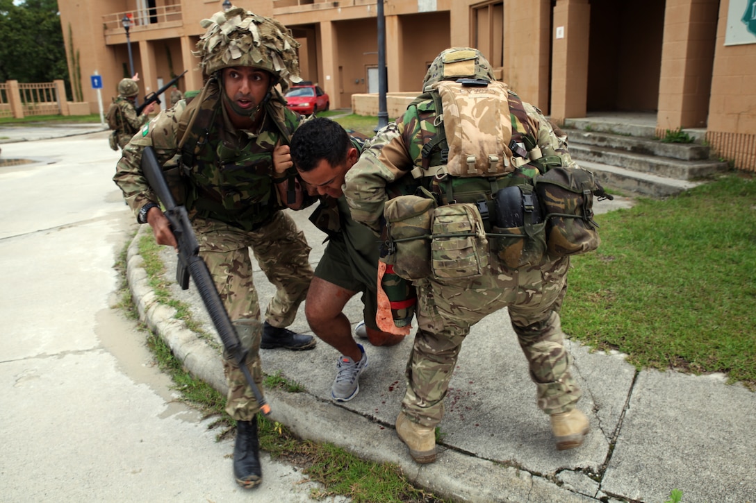 British Lance Cpl. Dhilushka U. Maheswaran (left), a military intelligence operator for 7 Military Intelligence Battalion, 1 Intelligence Surveillance Reconnaissance Brigade, and native of Abergavenny, Wales,  helps another British soldier carry  Sgt. Erick J. Velazquez (center), a geospatial intelligence analyst for 2nd Intelligence Battalion, II Marine Expeditionary Force, and a native of Coral Springs, Fla., as part of a casualty assessment and treatment scenario during Exercise Phoenix Odyssey on Sept. 16, 2014. The day’s training focused on common battlefield injuries, casualty care in the field, and lifesaving procedures in combat. The two forces have been training in a Military Operations in Urban Terrain facility on Camp Lejeune as part of a week long, scenario driven, bilateral exercise.
