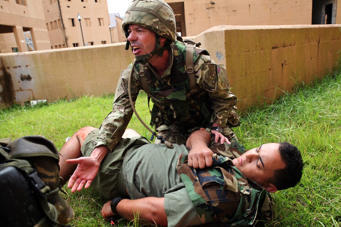 British Sgt. George P.H. Colquhoun,  a military intelligence operator and team medic for 7 Military Intelligence Battalion, 1 Intelligence Surveillance Reconnaissance Brigade, and native of Wallsend, England,  hollers for a tourniquet  while caring for Sgt. Erick J. Velazquez (center), a geospatial intelligence analyst for 2nd Intelligence Battalion, II Marine Expeditionary Force, and a native of Coral Springs, Fla., as part of a casualty assessment and treatment scenario during Exercise Phoenix Odyssey on Sept. 16, 2014. The day’s training focused on common battlefield injuries, casualty care in the field, and lifesaving procedures in combat. The two forces have been training in a Military Operations in Urban Terrain facility on Camp Lejeune as part of a week long, scenario driven, bilateral exercise.