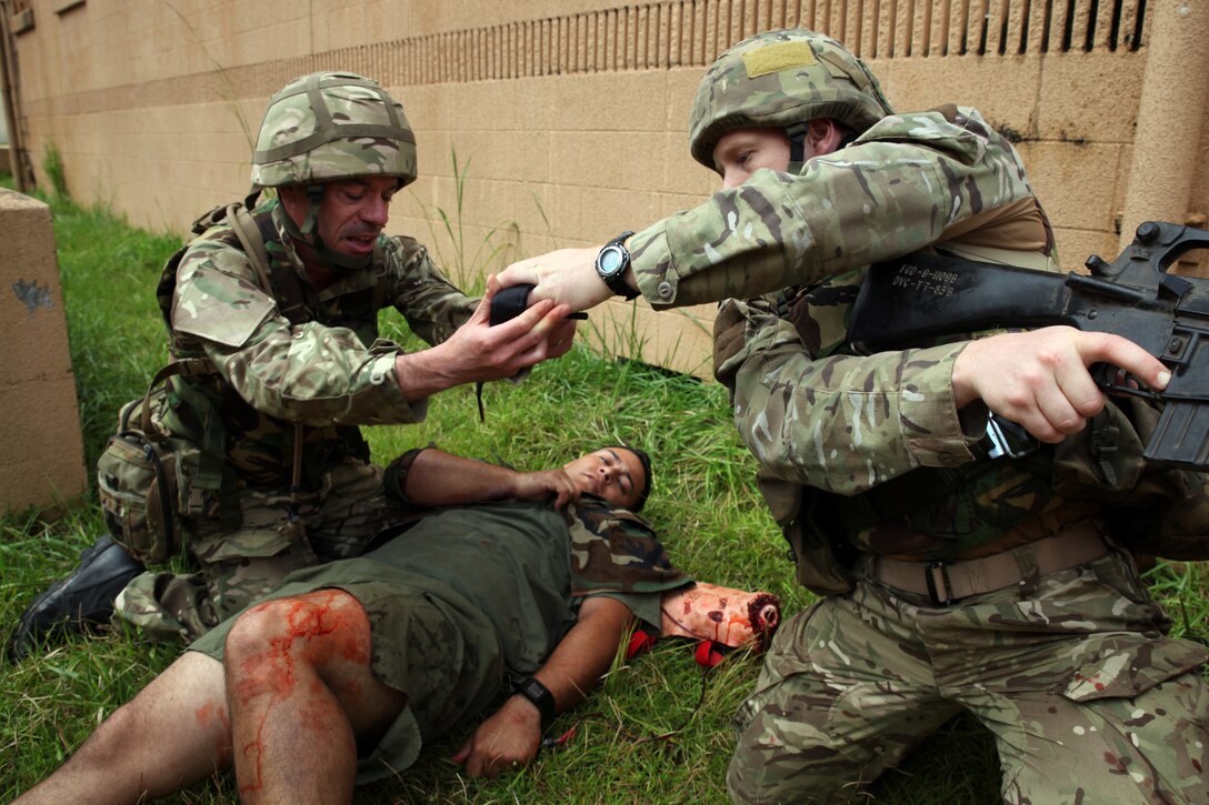 British Sgt. George P.H. Colquhoun,  a military intelligence operator and team medic for 7 Military Intelligence Battalion, 1 Intelligence Surveillance Reconnaissance Brigade, and native of Wallsend, England,  is handed a tourniquet  while caring for Sgt. Erick J. Velazquez (center), a geospatial intelligence analyst for 2nd Intelligence Battalion, II Marine Expeditionary Force, and a native of Coral Springs, Fla., as part of a casualty assessment and treatment scenario during Exercise Phoenix Odyssey on Sept. 16, 2014. The day’s training focused on common battlefield injuries, casualty care in the field, and lifesaving procedures in combat. The two forces have been training in a Military Operations in Urban Terrain facility on Camp Lejeune as part of a week long, scenario driven, bilateral exercise.