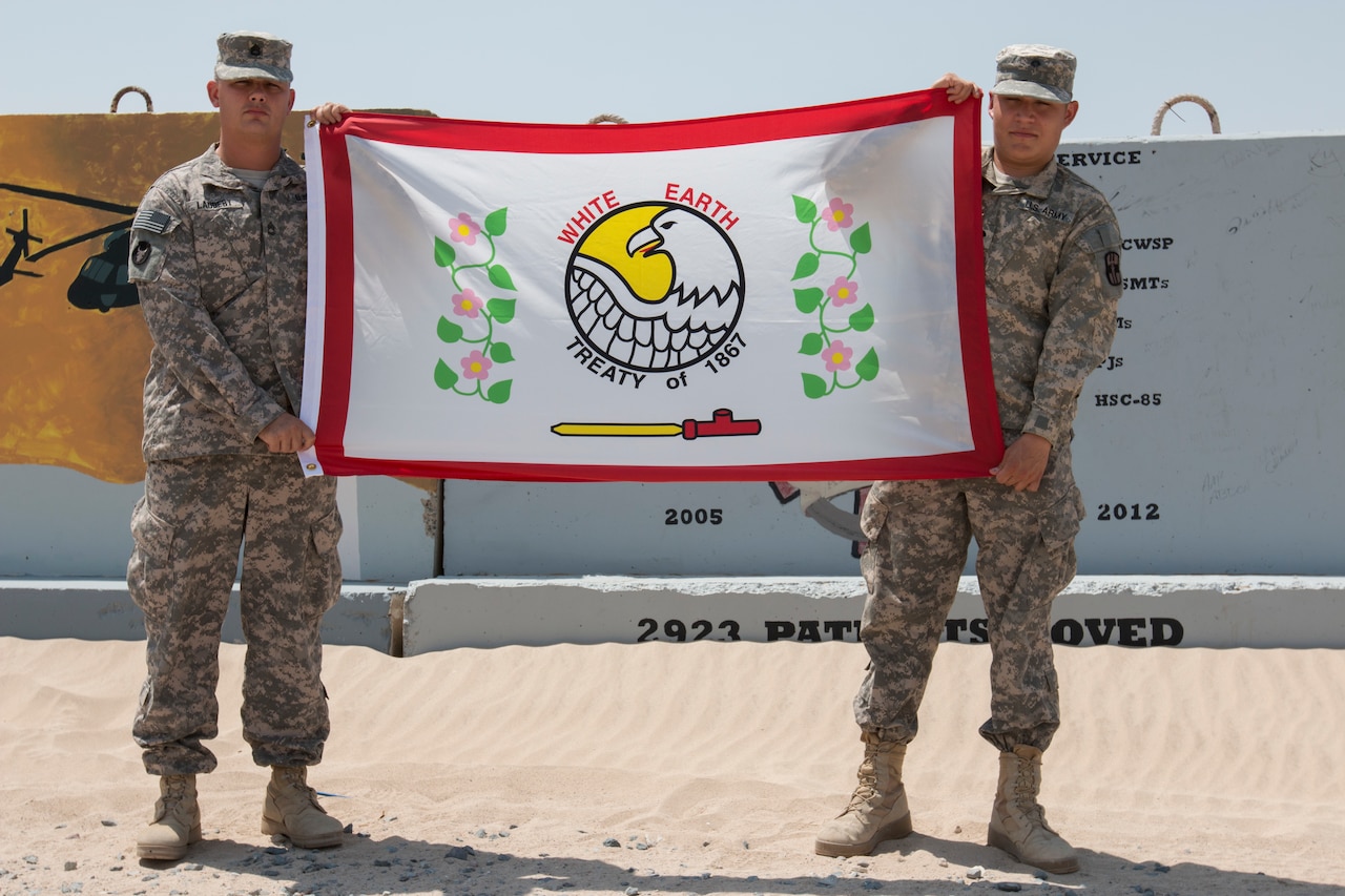 Army Sgt. 1st Class Laudert of the Minnesota National Guard’s 34th Combat Aviation Brigade and his brother, Army Spc. Cameron Laudert of the Army Reserve’s 452nd Combat Support Hospital, display the White Earth Nation flag while deployed to Camp Buerhing, Kuwait. U.S. Army photo by 1st Lt. Holly Elkin