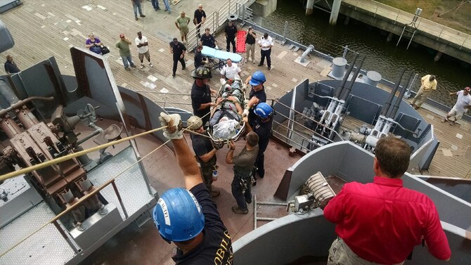 Two Air Force Special Tactics Airmen, standing on either side of the patient's head, work with local fire department officials to lower the patient off the USS Alabama during a rescue Sept. 17, 2014, in Mobile, Ala. The Special Tactics pararescuemen were part of a larger group conducting confined space rescue training on the USS Alabama when the individual fell approximately 25 feet while painting the ship. (Courtesy Photo/Released)
