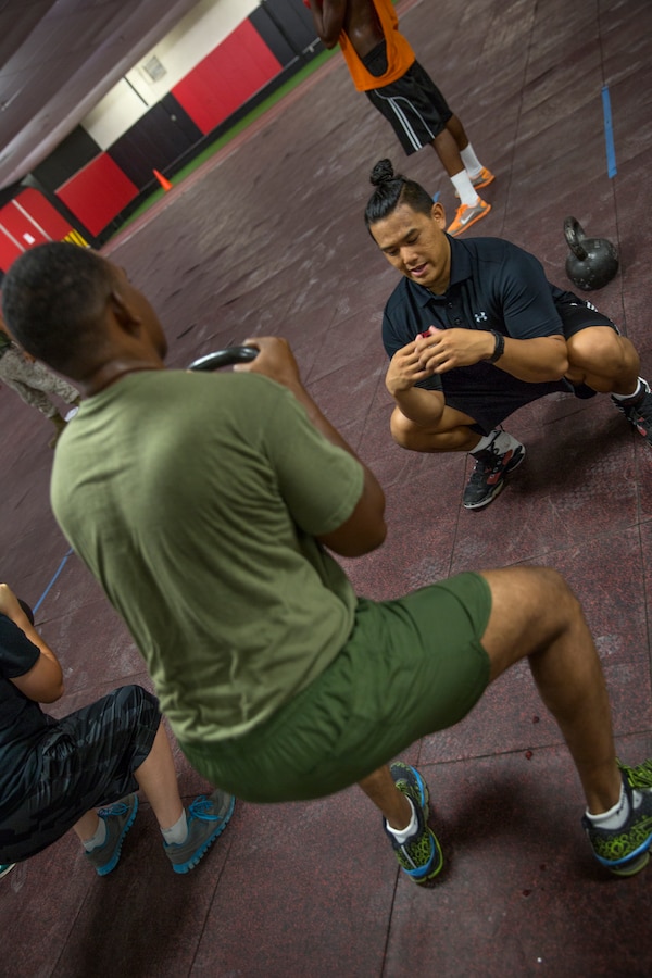 Randy Saldivar, a Return-to-Readiness program trainer, demonstrates proper form for a kettle bell squat during a lunch-time physical training session at the High Intensity Tactical Training Center aboard Marine Corps Air Station Miramar, Calif., Sept. 8. After Saldivar began working at the air station, he worked his way from being a personal trainer to being an RTR program trainer who helps people get back into shape after an injury.