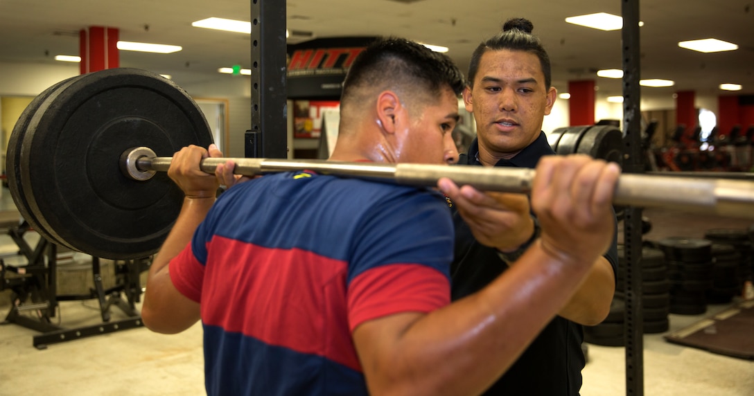 Randy Saldivar, a Return-to-Readiness program trainer, assists Cpl. Bryan Perez, an aviation supply specialist with Marine Aviation Logistics Squadron (MALS) 11, while he squats at the High Intensity Tactical Training Center aboard Marine Corps Air Station Miramar, Calif., Sept. 8. Saldivar's knowledge and understanding of the human body helps him teach proper form to people in the HITT Center. 