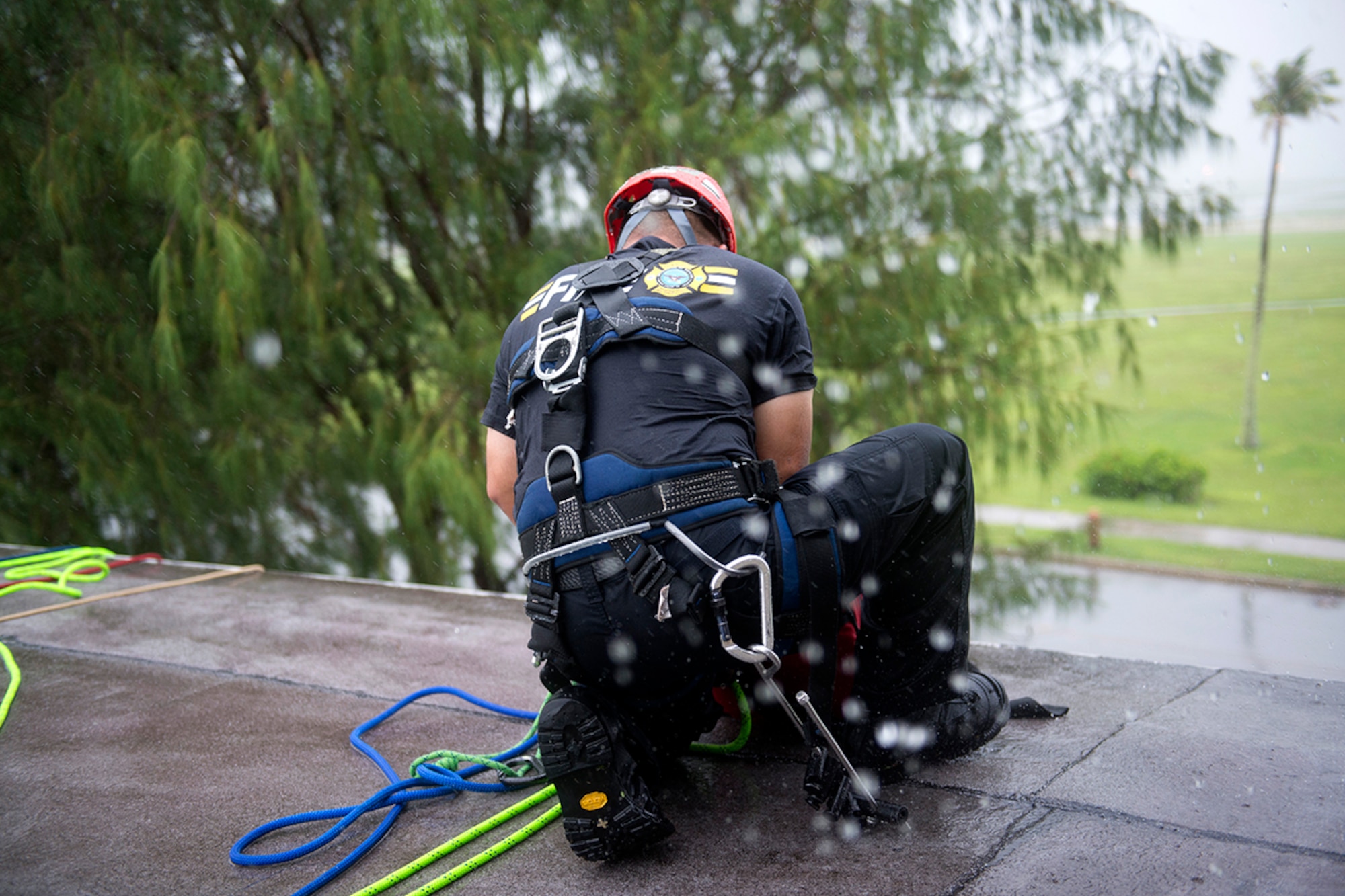 Ken Cruz, a Naval Base Guam firefighter, secures a rope to the edge to the roof in a downpour prior to rescuing a simulated victim during the Department of Defense Rescue Technician course event Sept. 16th, 2014, on Andersen Air Force Base, Guam. Thirteen firefighters from Andersen, Naval Base Guam and the Guam Fire Department attended the highly specialized training to learn elevated and confined space rescues. (U.S. Air Force photo by Tech. Sgt. Zachary Wilson/Released)