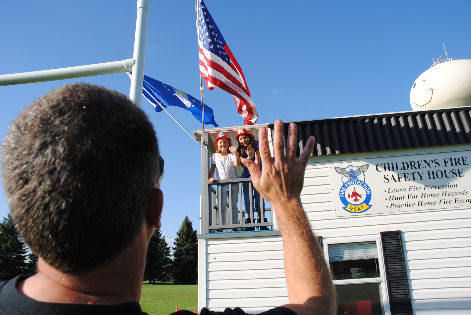 Grand Forks residents, Izzy and Zoe Cwikla wave to their father, Dan, from the small balcony of the Kids Fire Safety House during the Grand Cities Community Celebration, Sept. 15, 2014, on the grounds of the Cliff Fido Purpur Arena in downtown Grand Forks, N.D. The Kids Fire Safety House is used by the Grand Forks Air Force Base Fire Department to teach children fire prevention skills by hunting for home fire hazards and practicing fire escape drills.  (U.S. Air Force photo/Staff Sgt. Luis Loza Gutierrez) 
