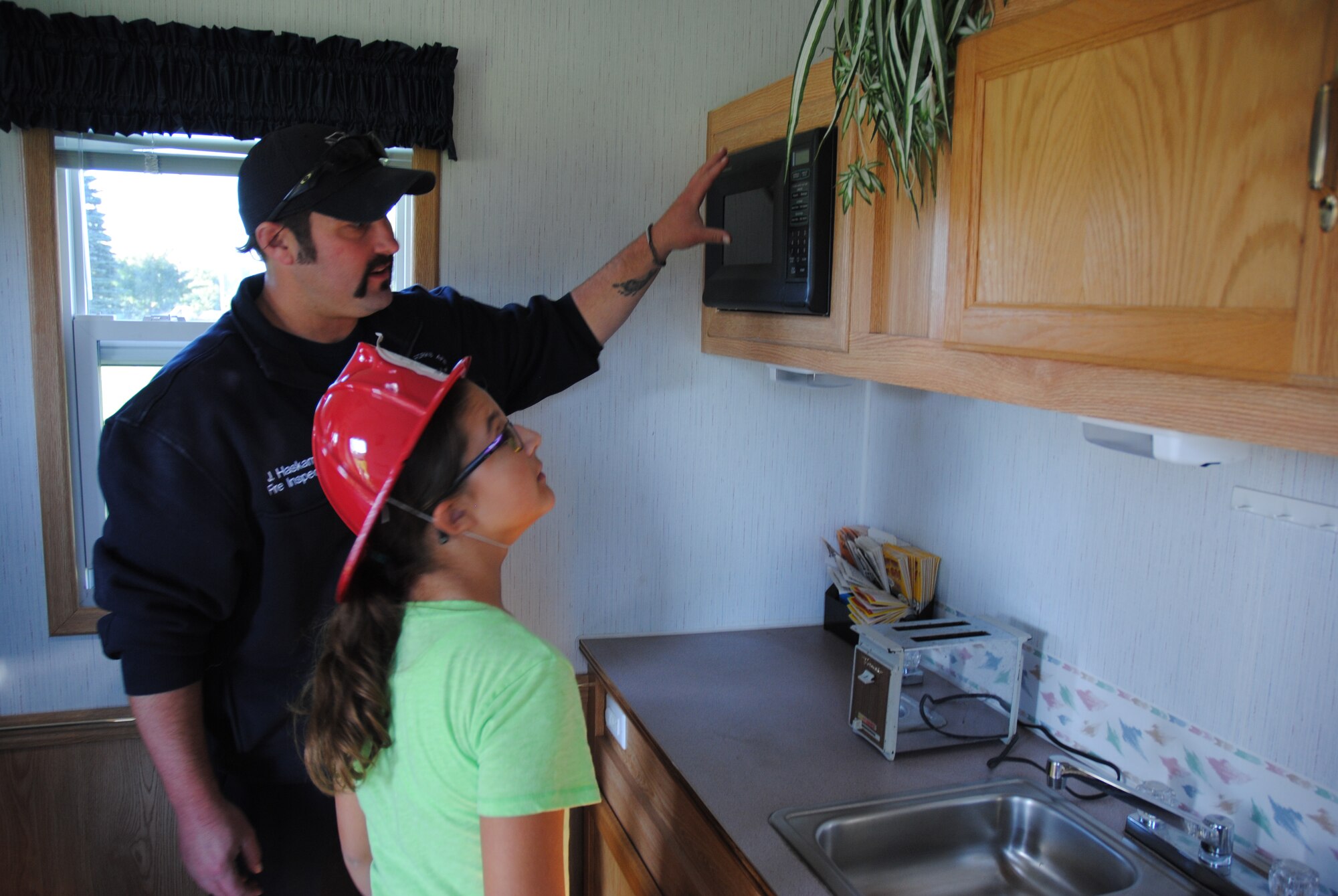 Air Force civilian fireman Justin Haskamp asks a young guest to identify as many fire hazards inside the small kitchen of the Kids Fire Safety House during the Grand Cities Community Celebration, Sept. 15, 2014, on the grounds of the Cliff Fido Purpur Arena in downtown Grand Forks, N.D. The Kids Fire Safety House is used by the Grand Forks Air Force Base Fire Department to teach children fire prevention skills by hunting for home fire hazards and practicing fire escape drills.  (U.S. Air Force photo/Staff Sgt. Luis Loza Gutierrez) 
