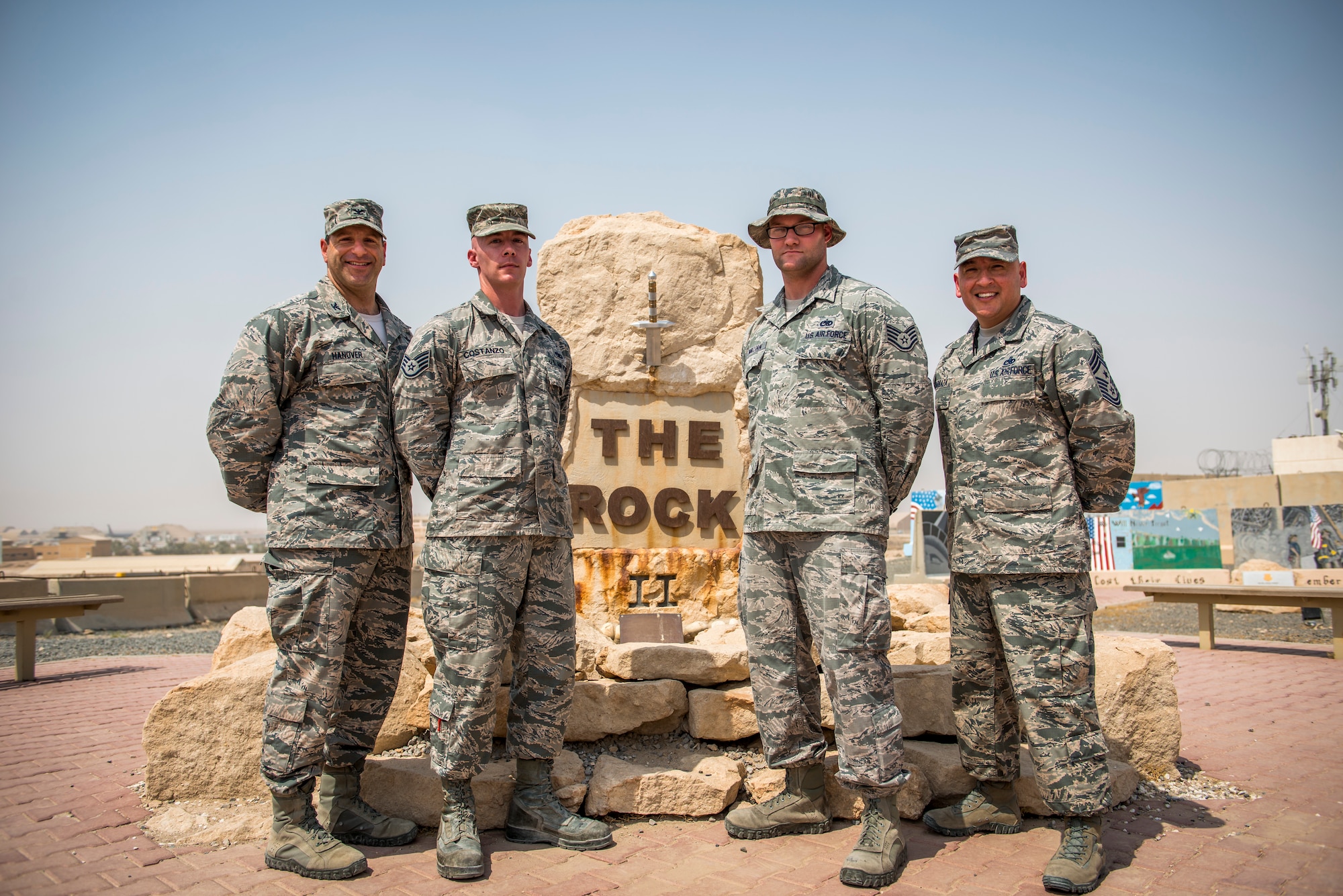 U.S. Air Force Staff Sgts. Justin Costanzo and Jarrod McMillian, 386th Expeditionary Maintenance Squadron aircraft maintenance technicians, pose in front of The Rock after unveiling the new sword to the 386th Air Expeditionary Wing with the commander, Col. Jason Hanover, and the command chief, Jose Barraza, Aug. 19, 2014 at an undisclosed location in Southwest Asia. Costanzo and McMillian spent over 140 man-hours designing and building the sword. Costanzo deployed from Shaw Air Force Base, S.C. and McMillian deployed from Davis-Monthan AFB, Ariz. in support of Operation Enduring Freedom. (U.S. Air Force photo by Staff Sgt. Jeremy Bowcock)