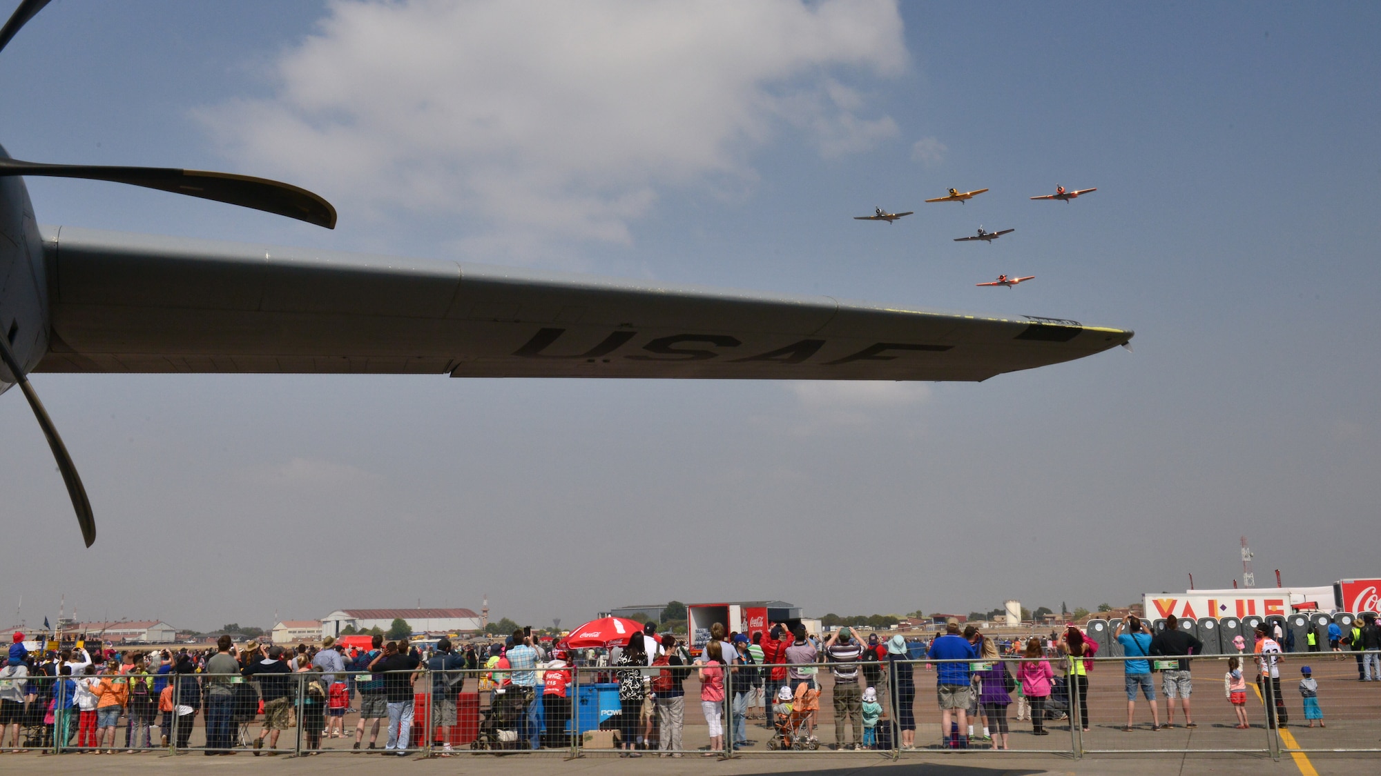 An aerial demonstration team flies over a crowd lined up to look inside a C-130J Super Hercules at the Africa Aerospace & Defence Expo at Waterkloof Air Force Base, South Africa, Sept. 20, 2014.  The C-130 was part of a total-force team of Guard, Reserve and active-duty Soldiers and Airmen at the expo. (U.S. Air Force photo/Staff Sgt. Travis Edwards)