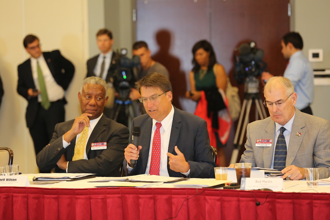 Cornell Wilson, left, sits with Governor Pat McCrory, center, and Bud Martin while McCrory addresses a room of state dignitaries and leadership from Marine Corps Air Station Cherry Point, N.C., and 2nd Marine Aircraft Wing at Miller’s Landing Sept. 16, 2014. Wilson is a retired Marine Corps major general and the current military affairs advisor to Governor McCrory. McCrory is the governor or North Carolina. Martin is the chairman of the North Carolina Military Affairs Commission.