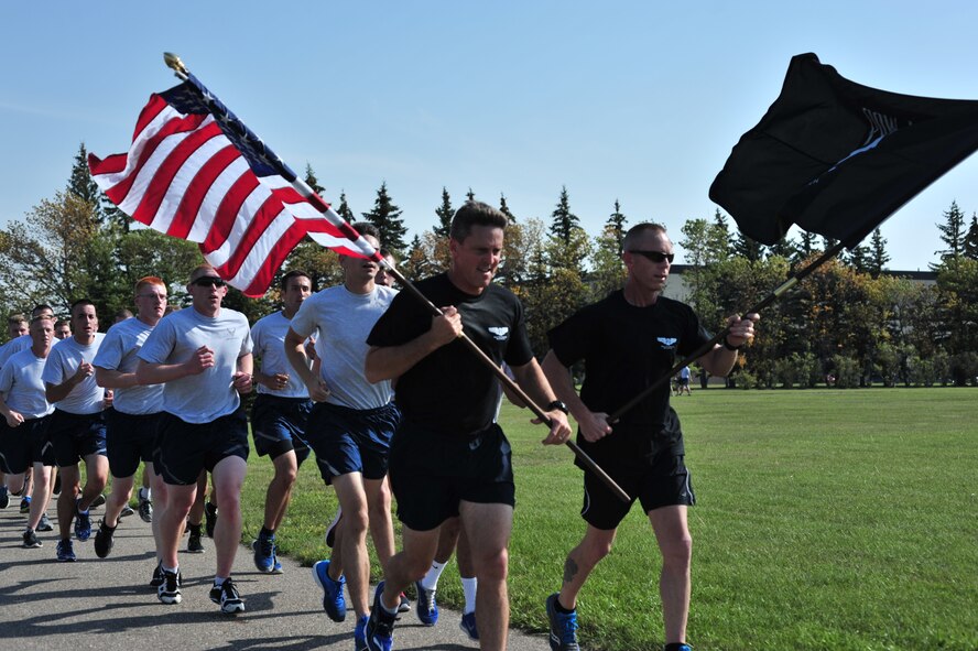 Col. Jason Armagost, 5th Bomb Wing commander, and Chief Master Sgt. Geoff Weimer, 5th BW command chief,  run with the U.S. Flag and the Prisoner of War and Missing in Action Flag during a 24-hour commemoration run on Minot Air Force Base, N.D., Sept. 19, 2014. During the run, Team Minot ran a total of 9,244 laps around the track to honor those held in captivity and those who have yet to return home. (U.S. Air Force photo/Senior Airman Malia Jenkins)